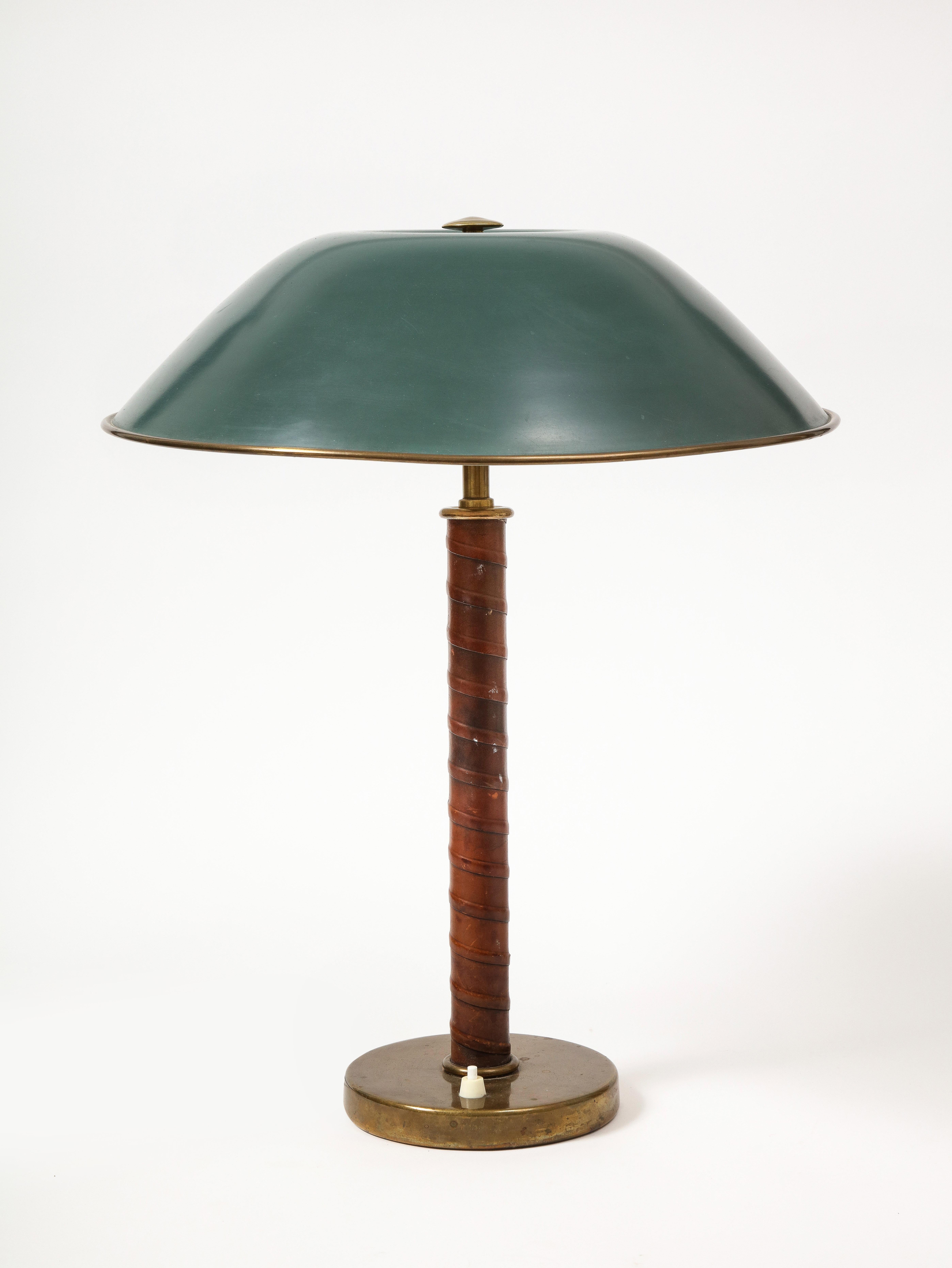 Refined leather, brass, and lacquered brass Swedish Grace table lamp, made by Bohlmarks. This lamp features a wrapped leather body and large beautifully patinated green shade.