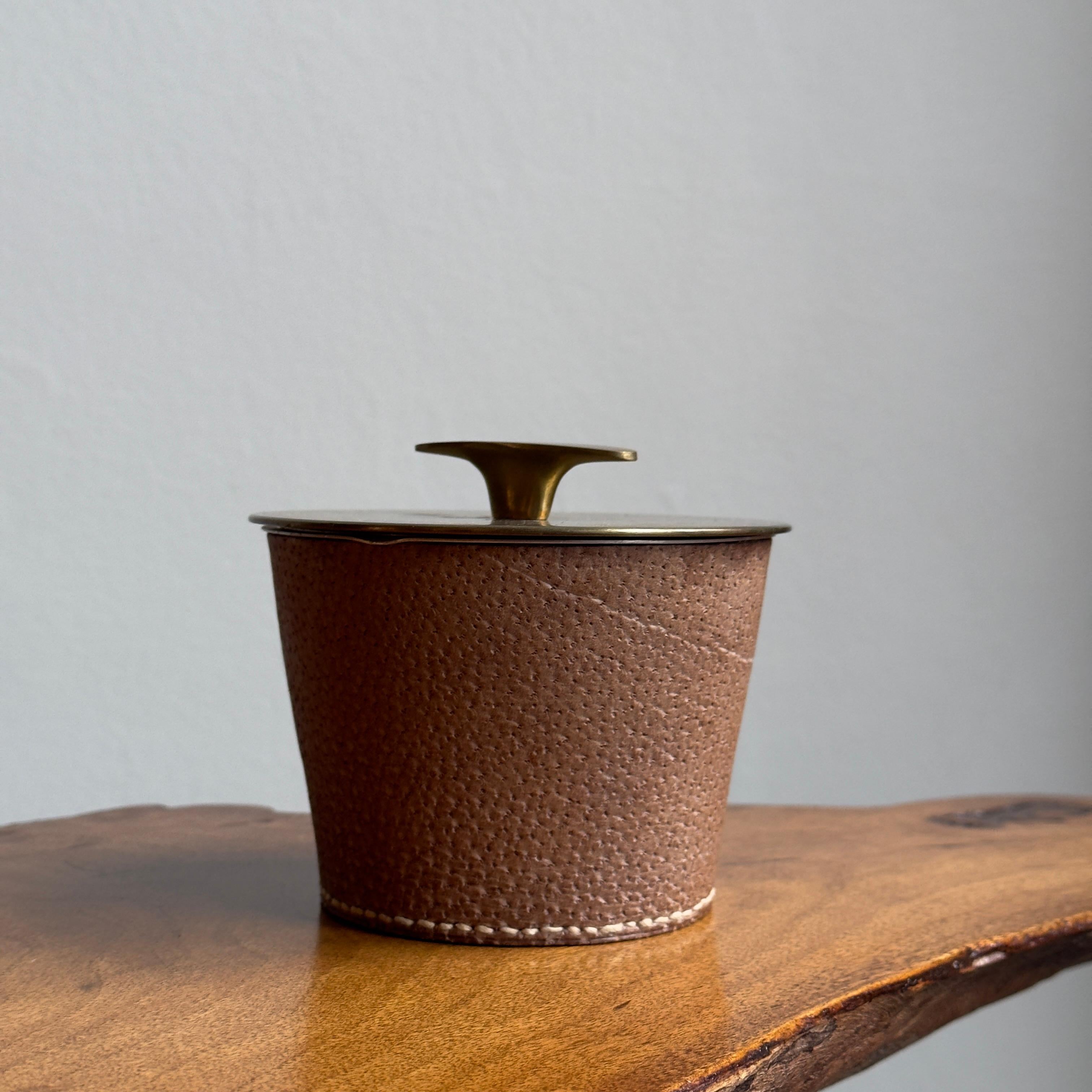 A leather-clad, brass-lidded humidor, designed by Carl Aubock II during the 1950s. 

The combination of brass and leather is typical of the designs by the second-generation Carl Auböck. A student of the Bauhaus under the tutelage of Joannes Itten,