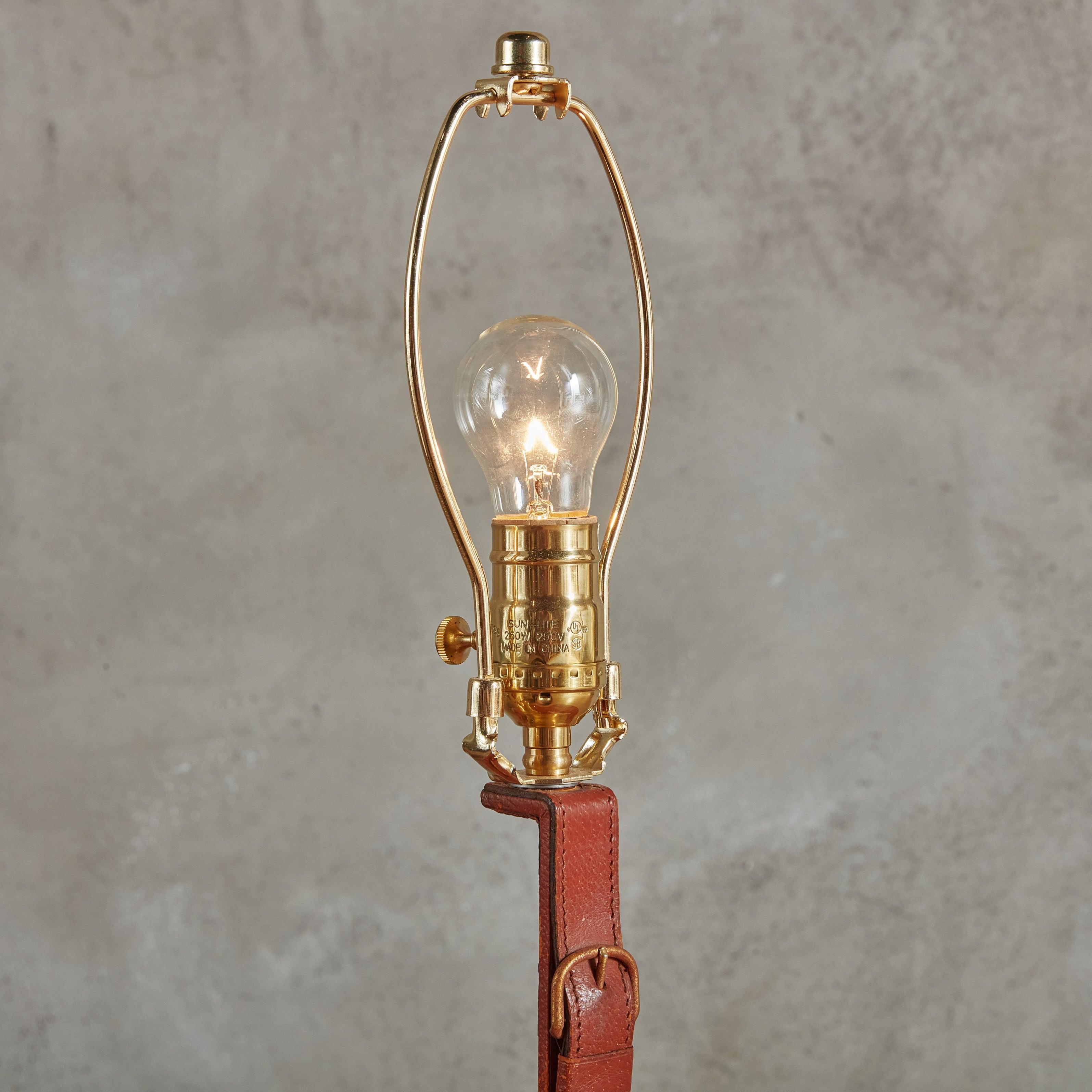 Eine französische Tischlampe aus den 1950er Jahren, entworfen von Longchamps Paris. Diese Lampe verfügt über einen Steigbügel aus massivem Messing, der in cognacfarbenes Leder mit Sattelnaht eingewickelt ist. Eine Messingschnalle ergänzt das Design