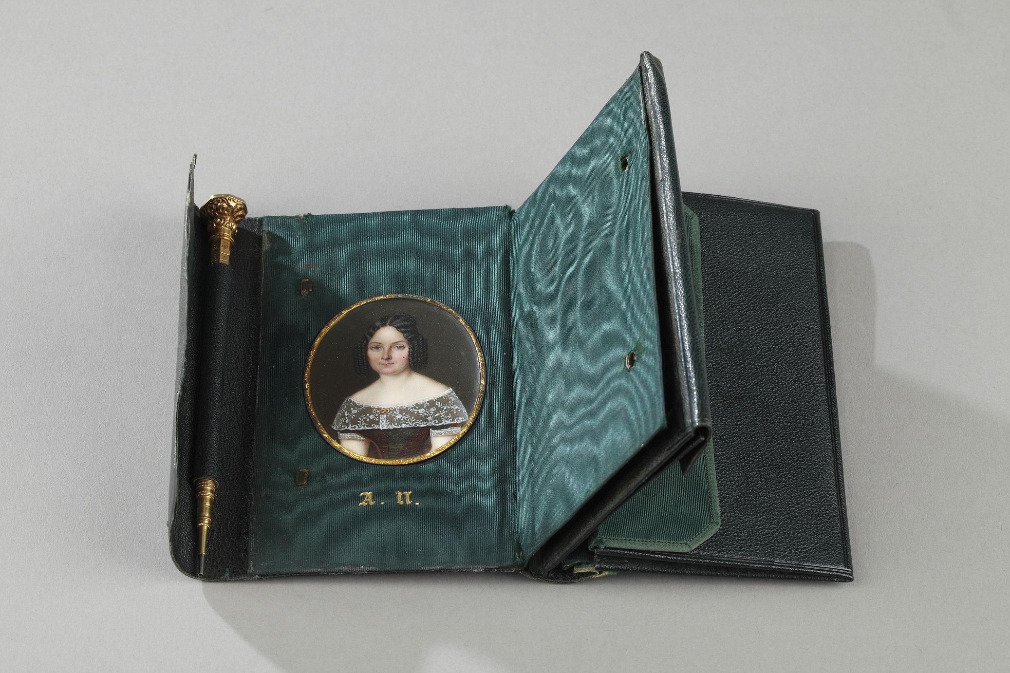 Green leather case with several gussets and bound sheets. The case opens with a gold clasp. Inside the case, an oval miniature is preserved. This represents a young woman in bust wearing a dress and lace scarf adorned with a brooch. The miniature is