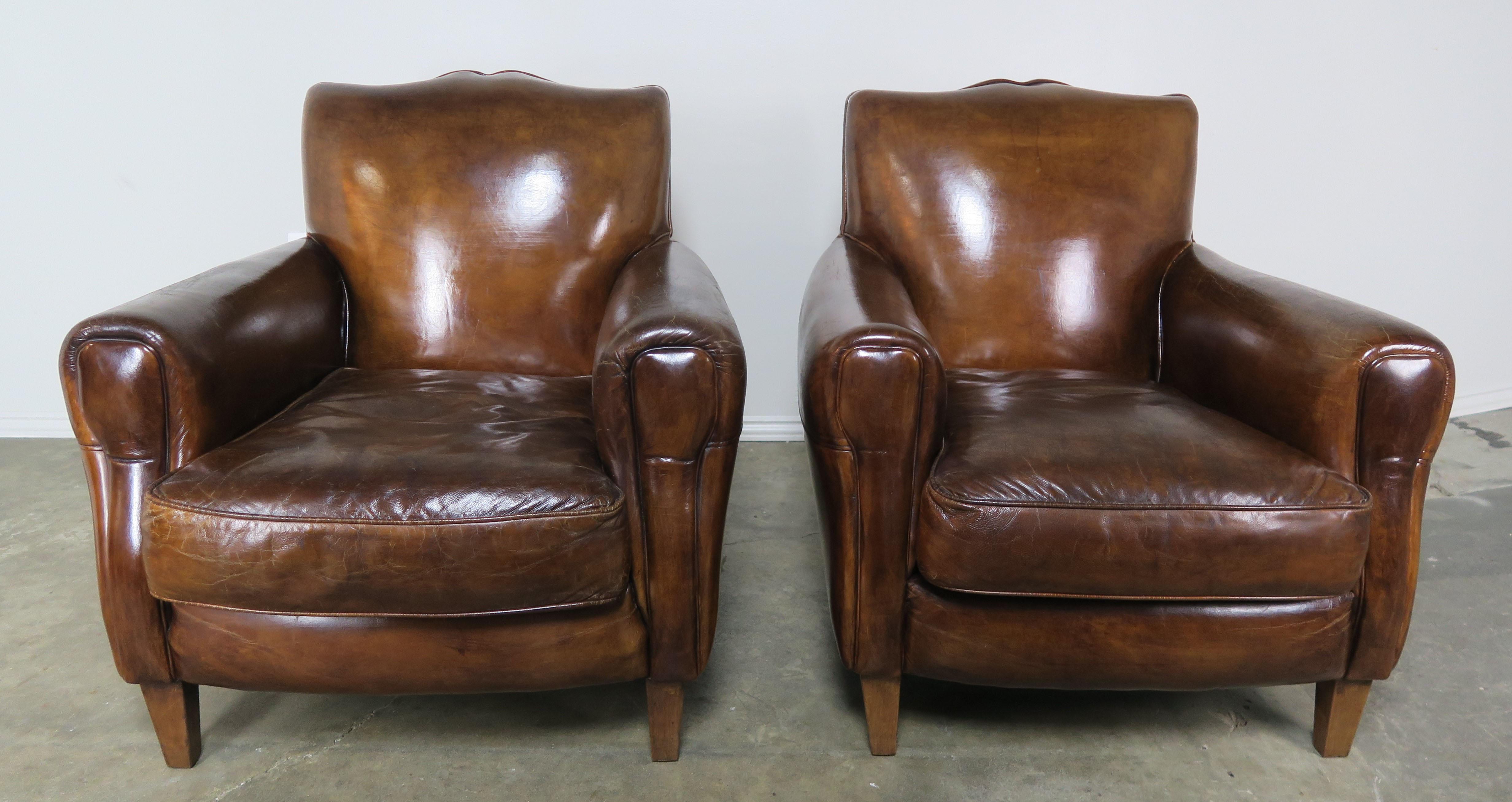 Pair of handsome French deco style mustache-shaped club chairs with loose seat cushions. The leather is a beautiful shade of tobacco and in excellent overall condition. Baseball stitching and self-piping throughout. The armchairs stand on four