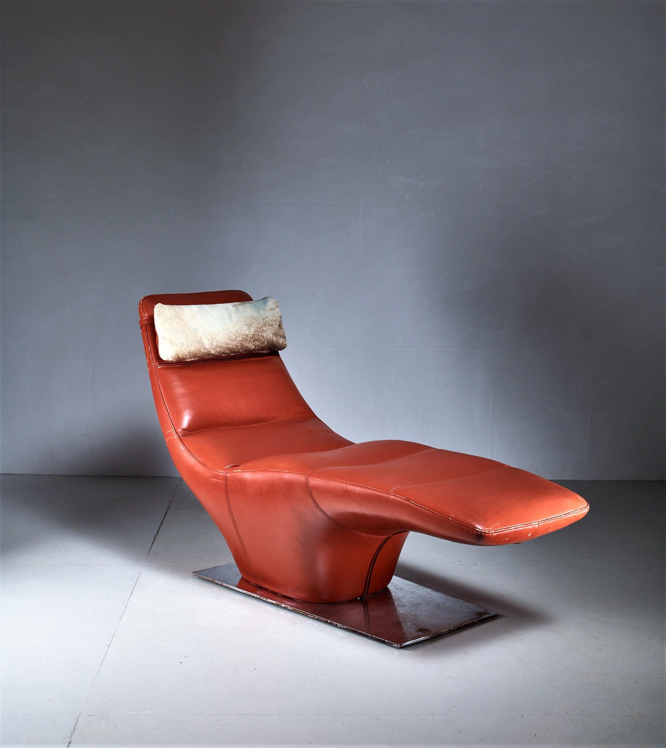 A Mid-Century American chaise longue standing on a stainless steel base. The chair has a light brown leather upholstery and has a removable partly cowhide pillow.