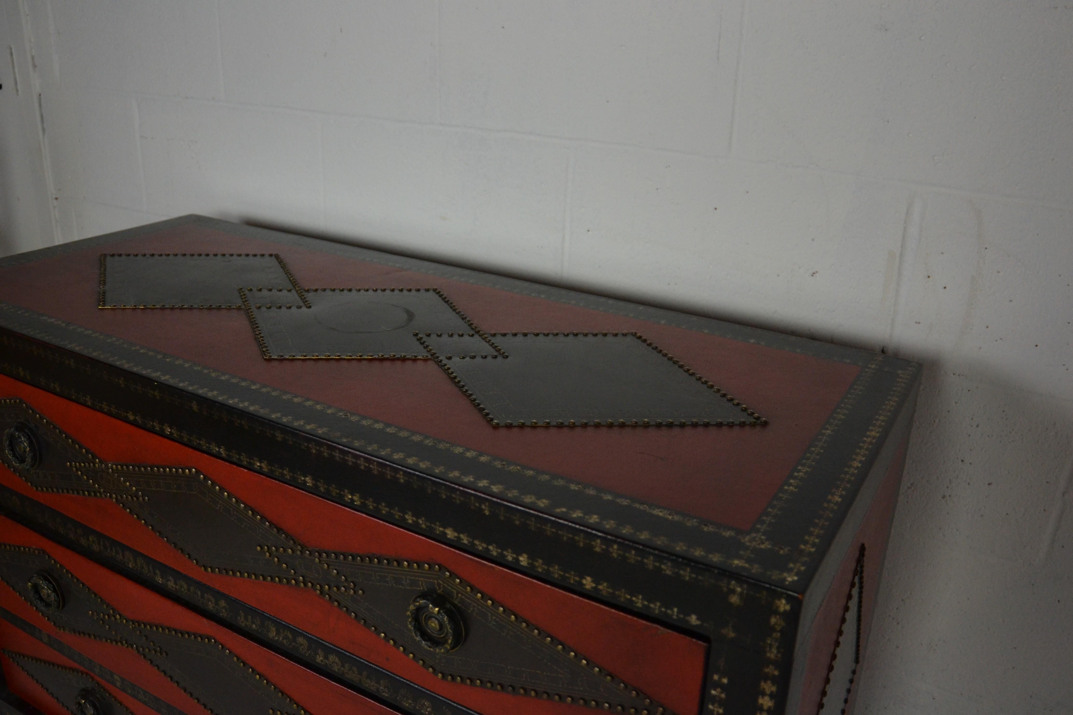 Chest of drawers clad in black and red leather. The applied diamond-shaped panels are in metal with a dark patina and edged with metal studs. Probably copper or brass. The edges of the chest are tooled-leather. Even the top drawer edges are tooled