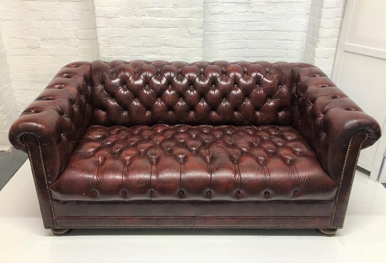 Leather Chesterfield style loveseat / sofa. The sofa is burgundy with wood bun feet.