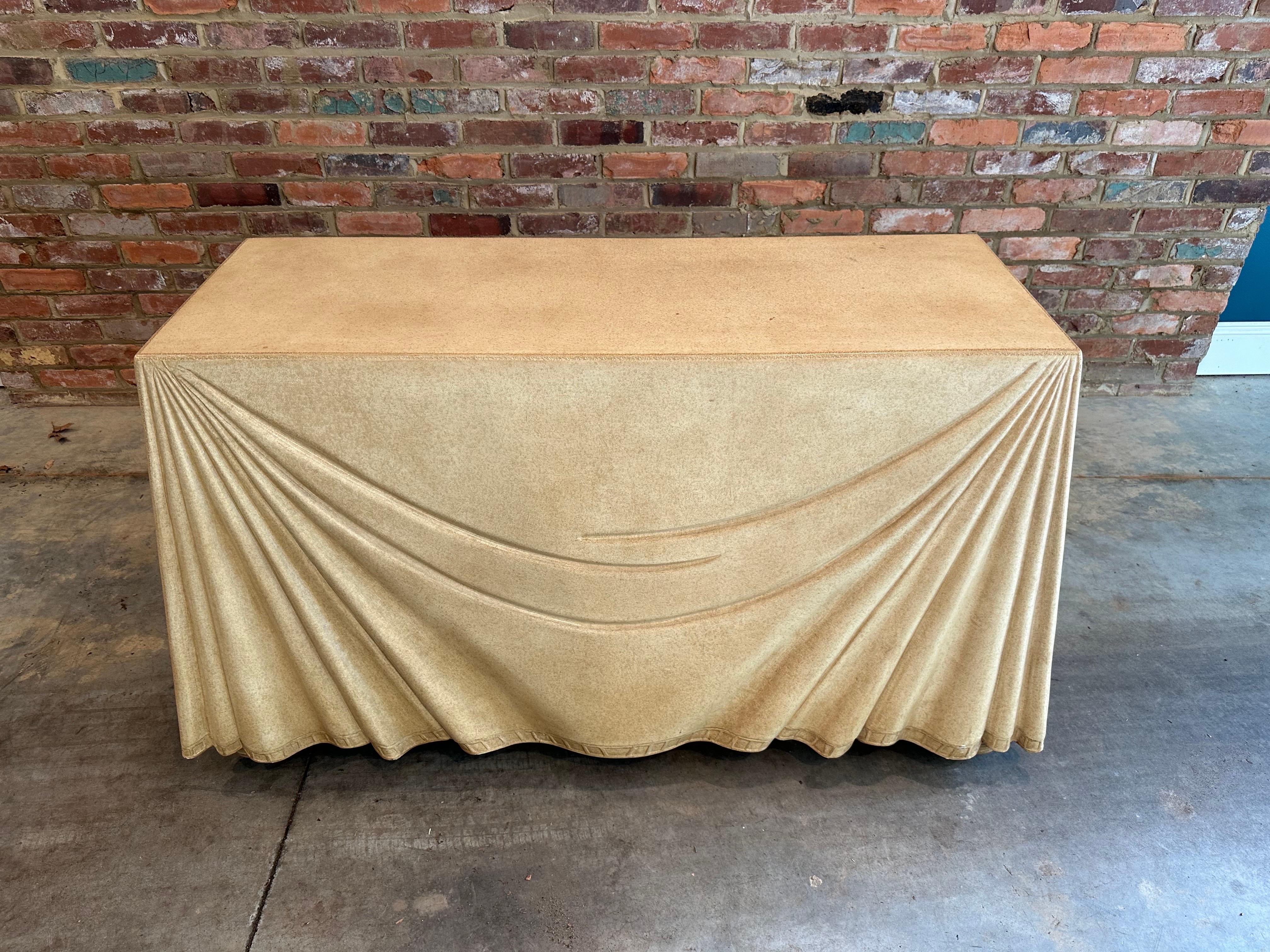 Elegant trompe-l'œil leather-clad console table, circa mid-1980 by Marge Carson. Deep camel-colored tone with ribbon-look banding at bottom and scroll detail around edges. Table rests on barely visible bun-shaped feet. Table includes small shelf