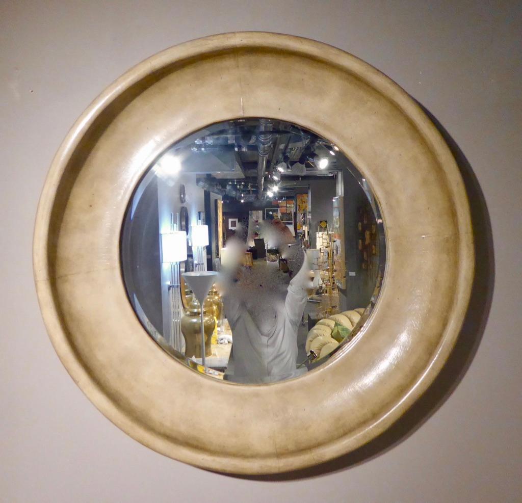A large leather-covered circular mirror, attributed to Maitland Smith, circa 1970s. The mirror plate has a beveled edge and the putty colored leather is in excellent, original condition.