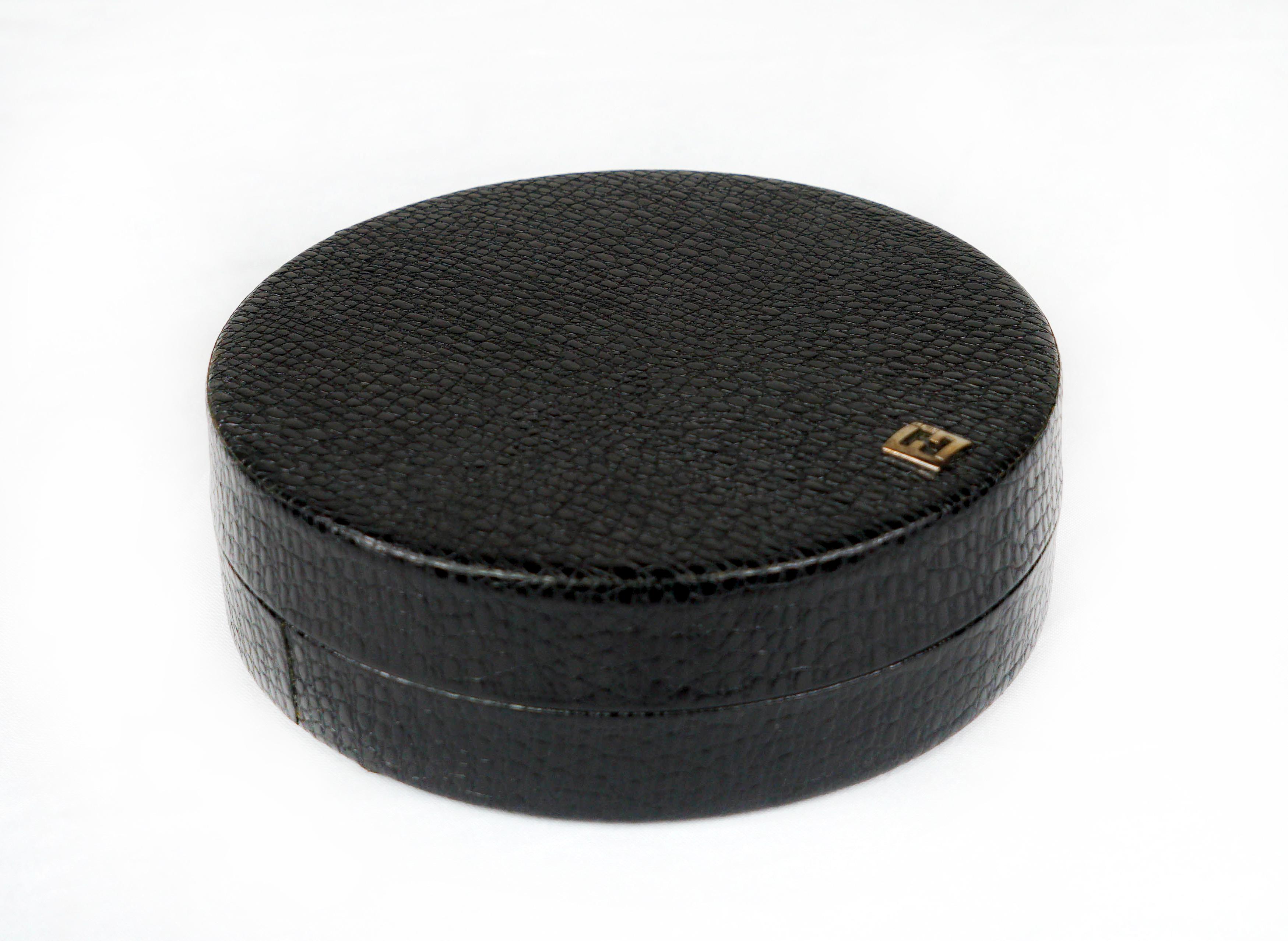 Eine elegante Schachtel aus Metall, bezogen mit schwarzem Leder mit Krokodilprägung und ausgekleidet mit schwarzer Mikrofaser. Das Oberteil ist mit dem klassischen Fendi FF Logo aus Metall verziert.
  