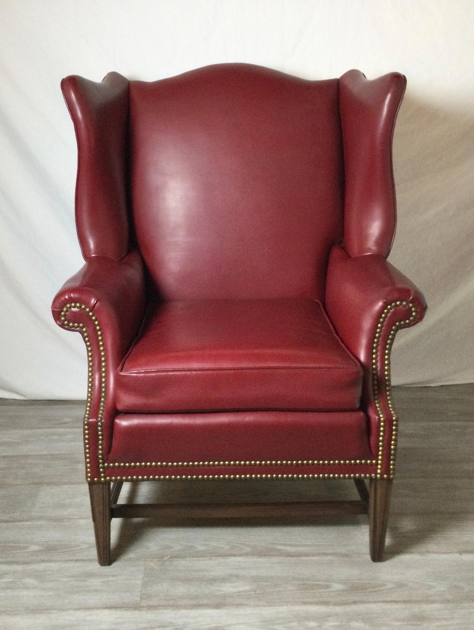 A large and comfortable Cordovan leather shapely Devon style wing chair. The large back with flared wings with a loos leather cushion seat with brass nail head trim. The exposed legs are mahogany. Made in the mid 20th century by Hickory Chiara.