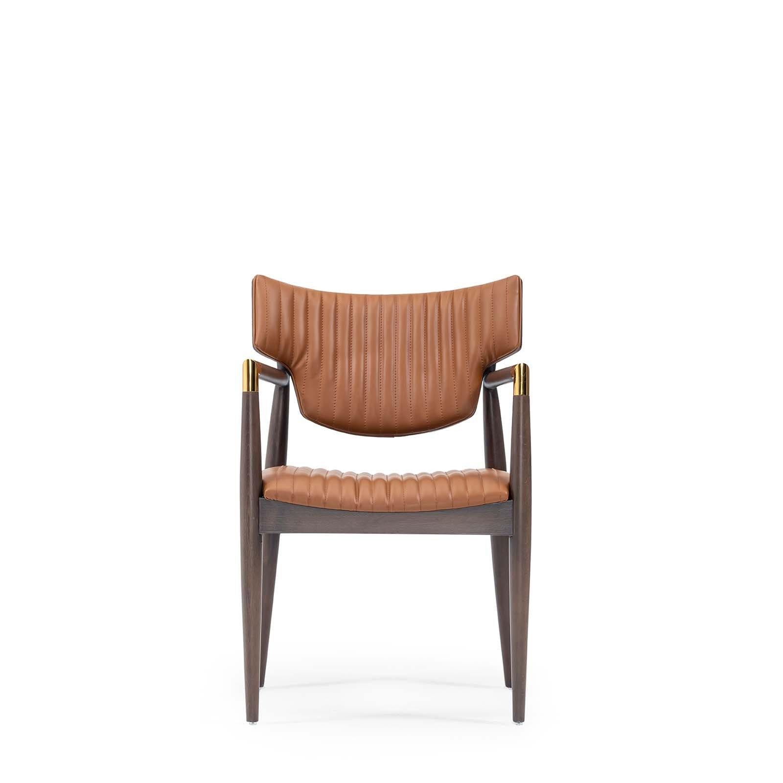Contemporary chair with armrests, solid beech structure in walnut finish.
Expertly stitched with a modern channel design, this striking arm chair invites comfort with its supple leather. Rounded wood frame with gold detailing on the arms creates a