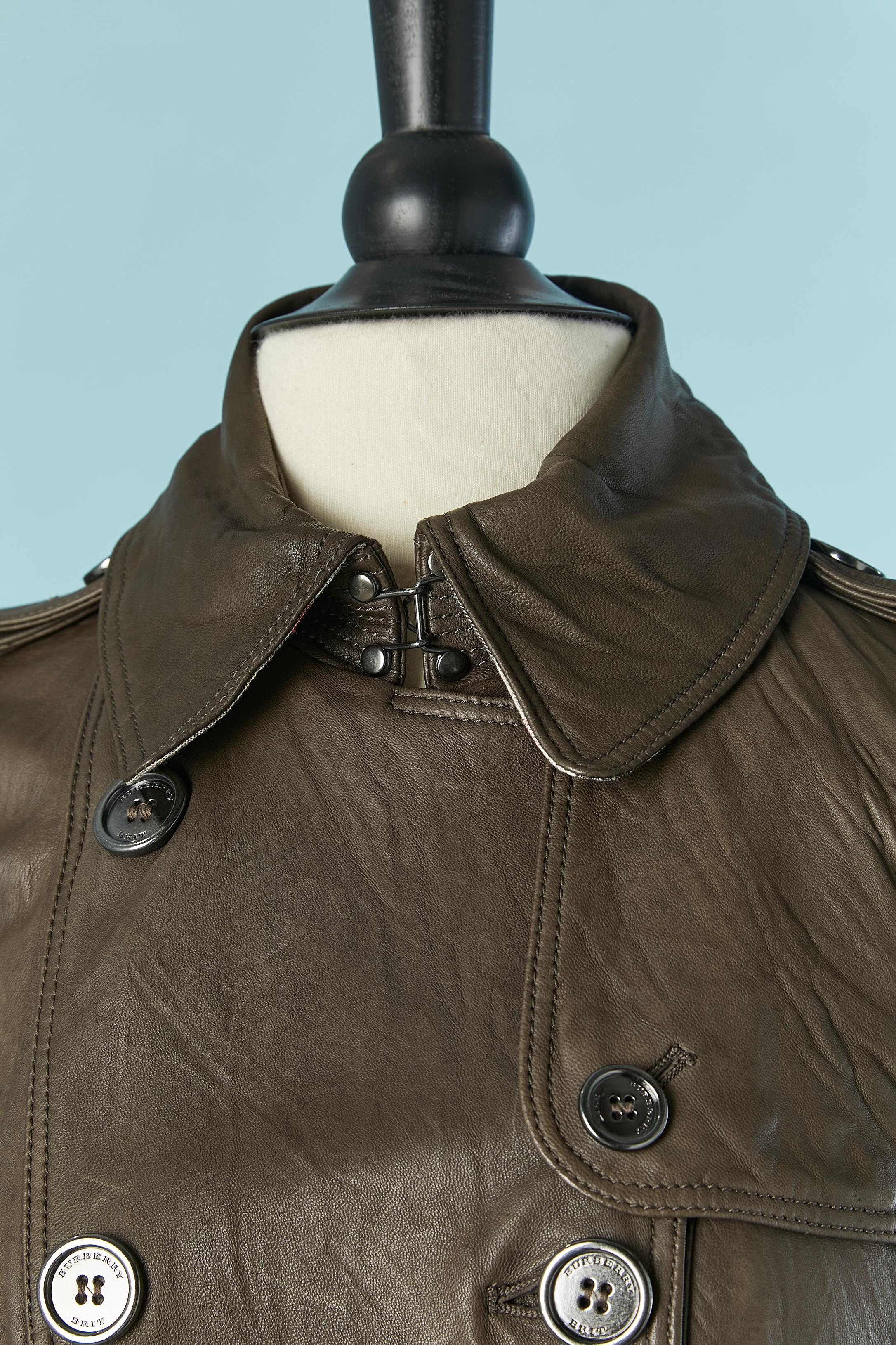 Leather double-breasted trench coat . Check cotton lining ( on the top of the body ) and rayon lining underneath. Leather belt and buckle closure. Branded button and buttonhole closure on the middle front. Pocket on both side with branded button and