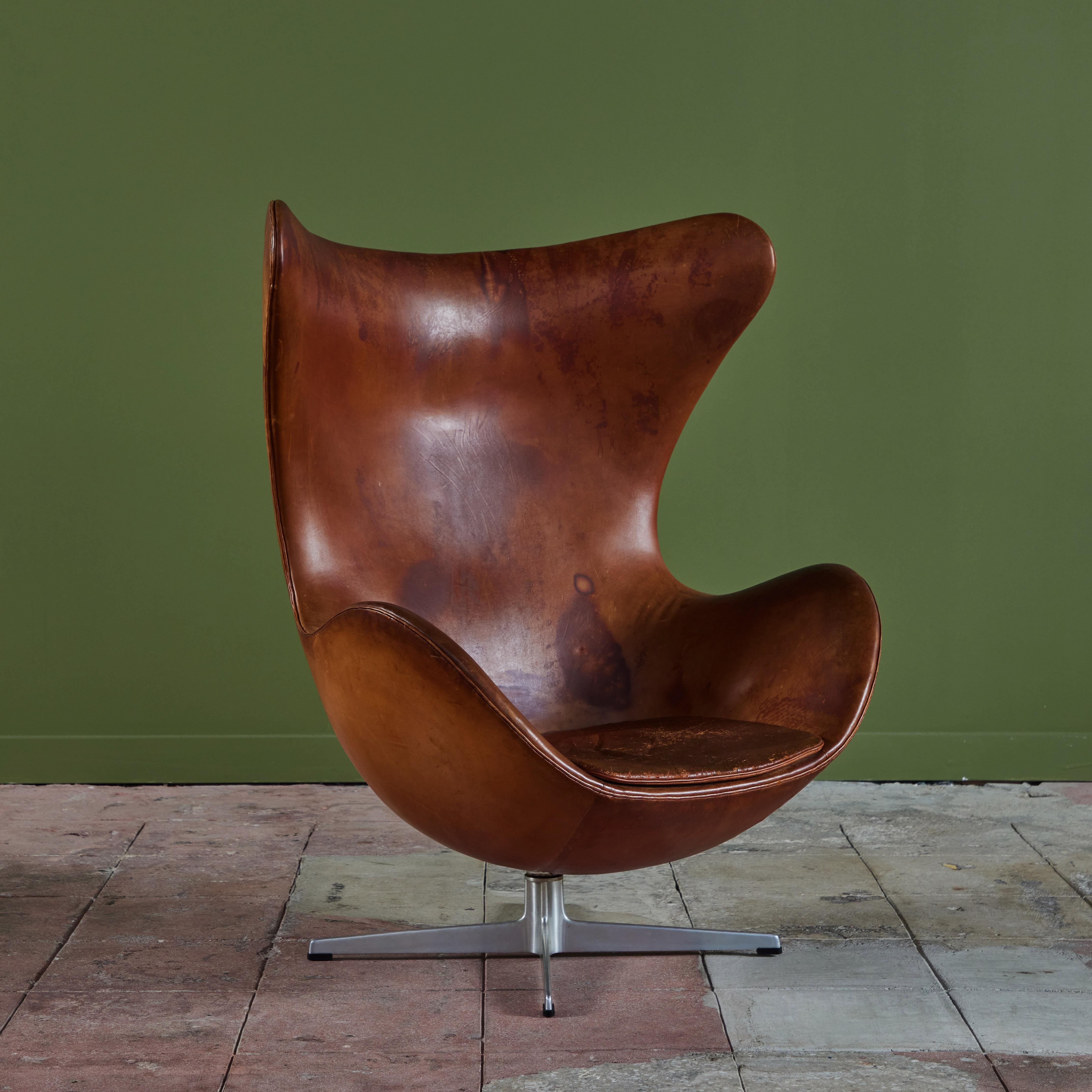 The iconic, Arne Jacobsen-designed egg chair, c.1960s, Denmark. The chair features its original rich saddle colored leather with its own distinctive patination. The high-backed chair has a seat cushion and swivels 360° on a four star aluminum base
