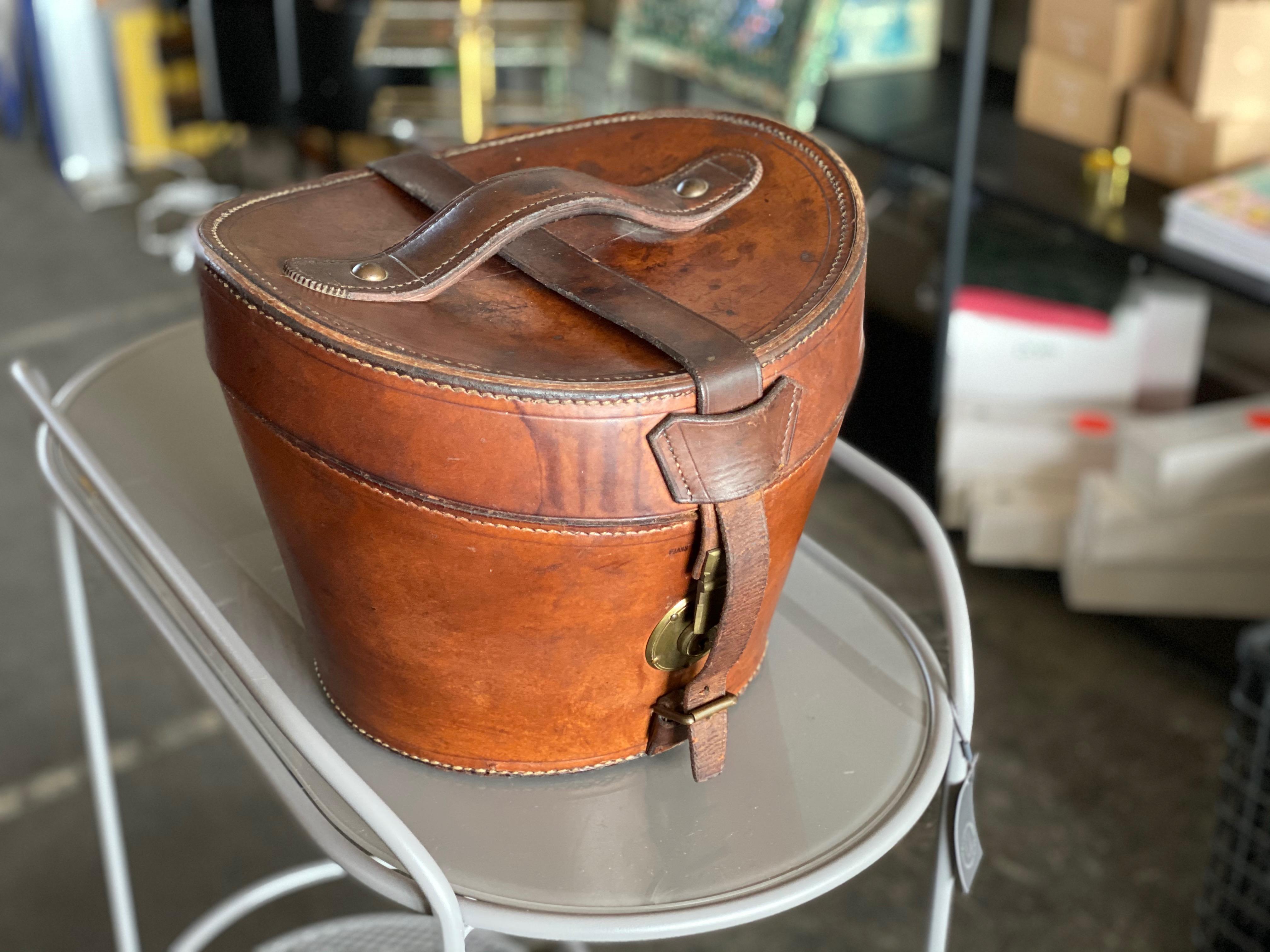 Old hat box from circa 1900, this rare hat box is made of leather with brass fasteners and is in good condition. The key to the lock is unfortunately not included, but the box can still be opened. From the inside it is lined with rust-colored