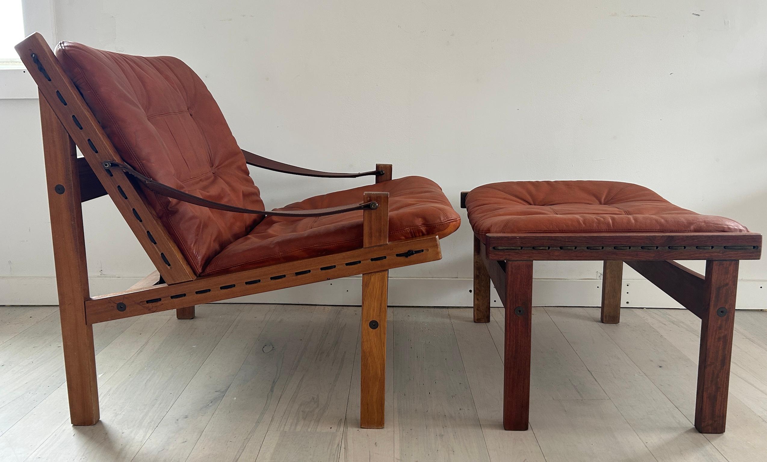 Burnt orange leather “Hunter” Safari low lounge chair with ottoman by Torbjørn Afdal for Bruksbo circa 1960. Solid wood frame with strung brown canvas back. Tan belt leather arms with brass hardware. Burnt orange leather seat and ottoman cushions.