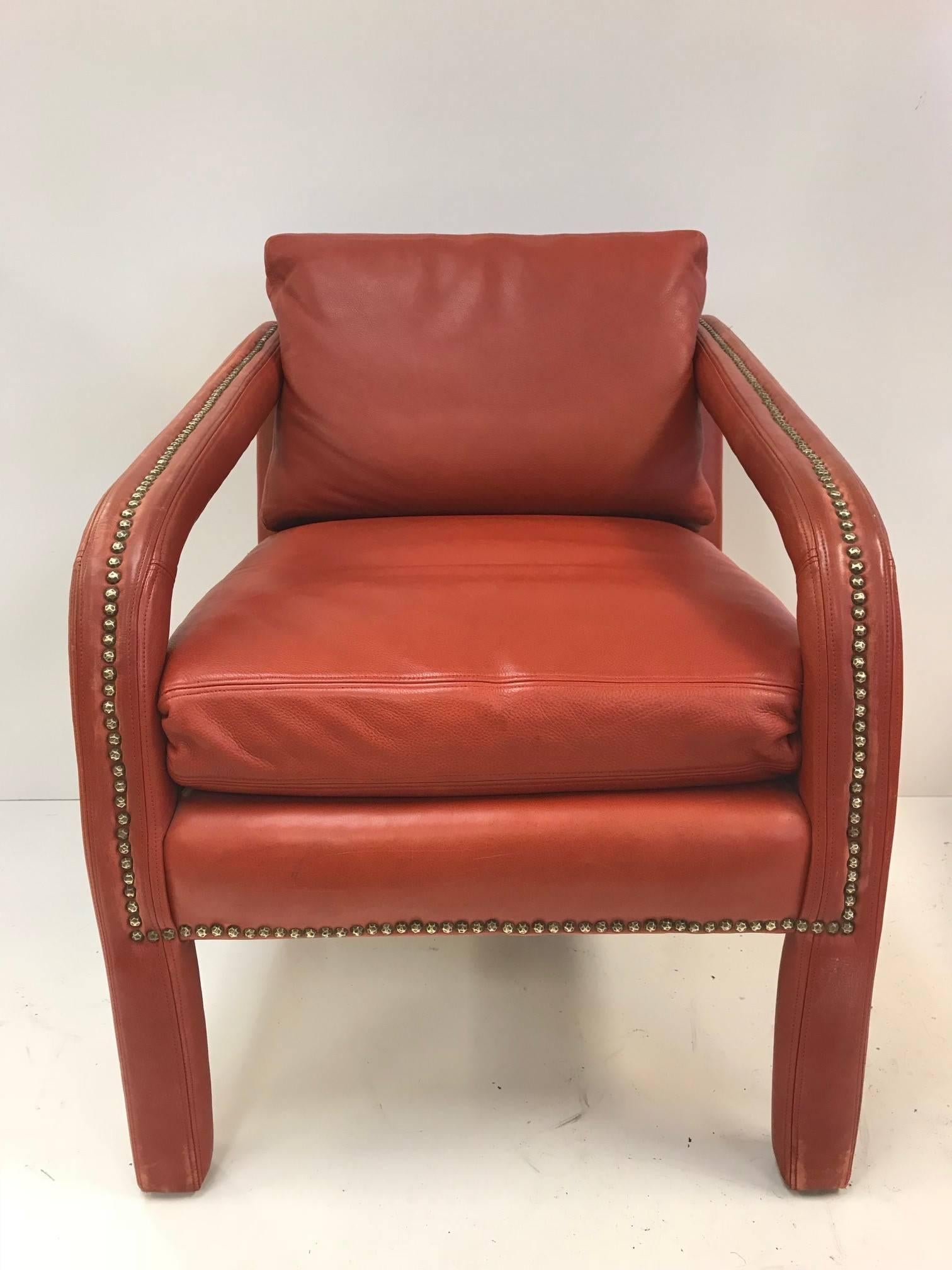 Mid-Century Modern leather lounge chair and ottoman. The chair has sloping arms with brass stud trim to the arms and ottoman. Gilbert Rohde Style.