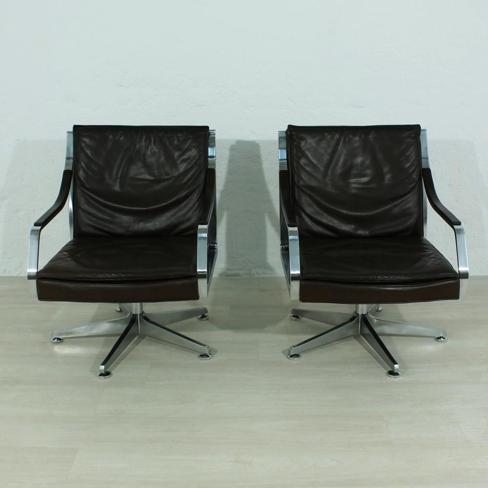 This pair of lounge chairs features brown leather upholstery and chromed steel frames. They have a rotating and tilting mechanism, and the feet are height-adjustable.