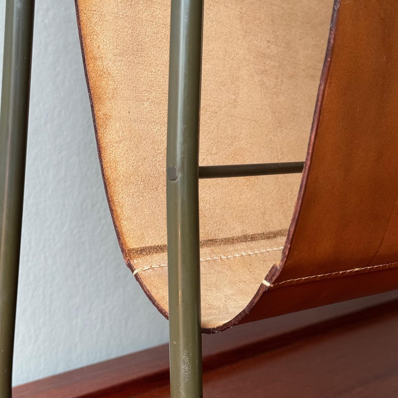 A leather magazine rack designed by Carl Auböck II during the 1950s.

Comprised of a tan leather sling and tubular brass armature, this magazine rack was designed and made by Carl Auböck II. The patinated brass frame of the rack provides a pleasing