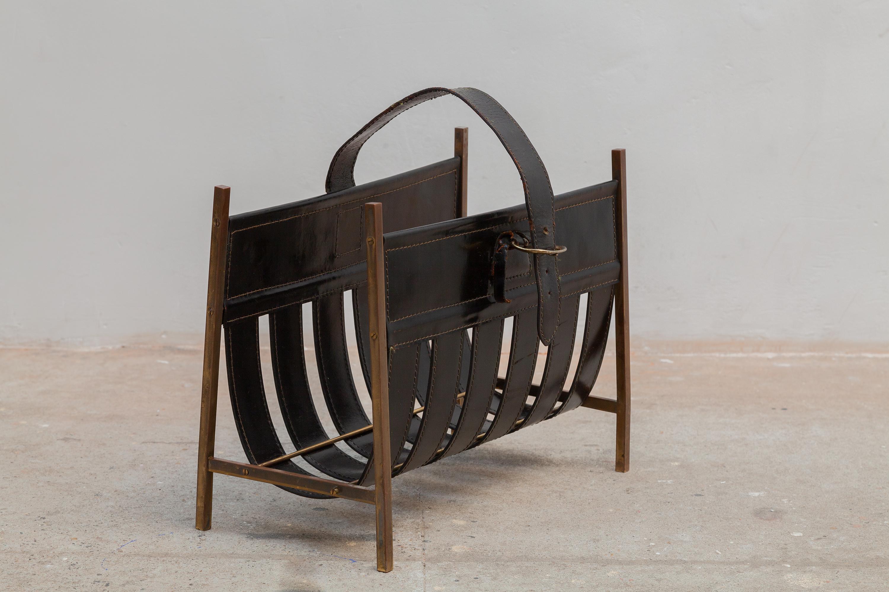 Vintage midcentury magazine rack or fireplace caddy. Metal frame with black leather sling and belt strap. 
Dimensions: 42 W x 33 H x 19 D cm.