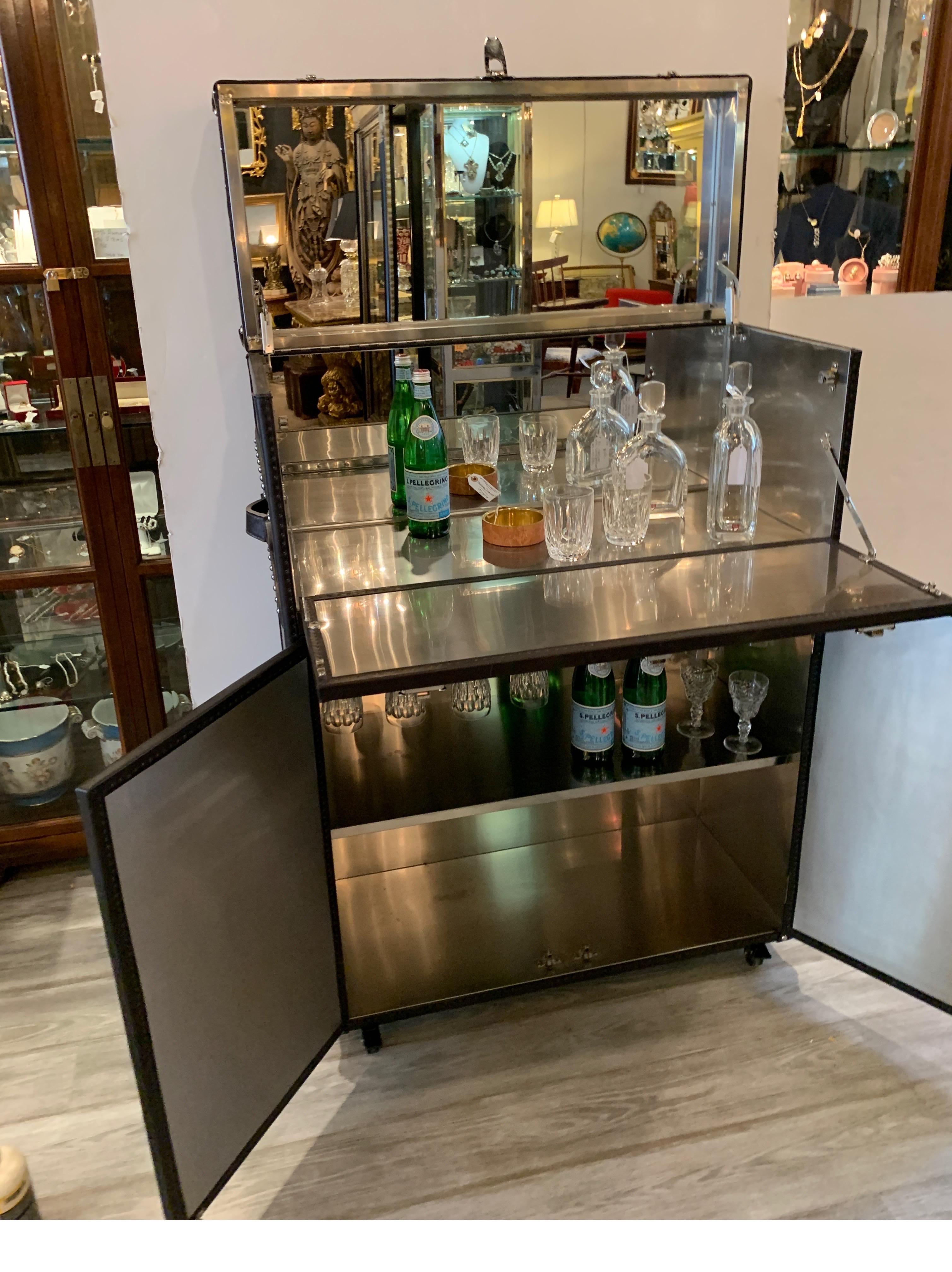 High style fold out bar with leather covering and polished nickel hardware. The top lifts to reveal a brushed steel interior with mirrored top. The lower section opens up to show a brushed steel lining with shelf and upper holders for stemware. The