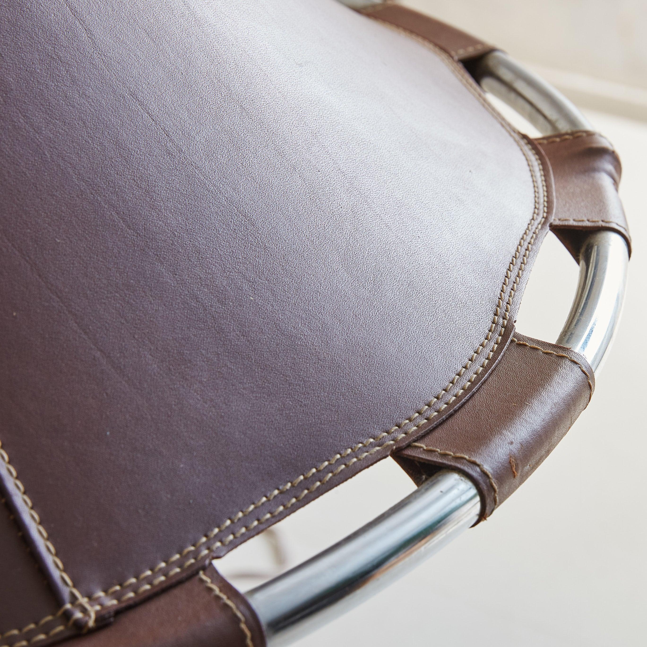 A 1970s Swedish pendant light featuring a circular chrome frame encircled by a rich, deep brown leather shade with stitch detailing. The design showcases an intriguing play of geometric forms, with the leather meticulously attached to the tapered