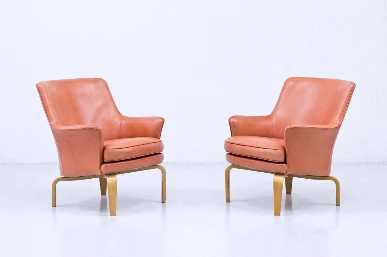 Pair of “Pilot” armchairs designed by Arne Norell in 1967. Manufactured by his own company in Sweden during the 1970s. Original faded red leather upholstery, laminated beech legs.