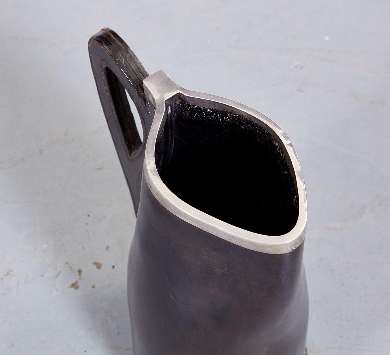 A sophisticated pitcher made of a continuous piece of patinated leather hide (with a stitched bottom piece) fastened with a thick stitched leather handle and bearing in this piece a substantial hallmarked silver rim.  Wonderful organic shape, and a