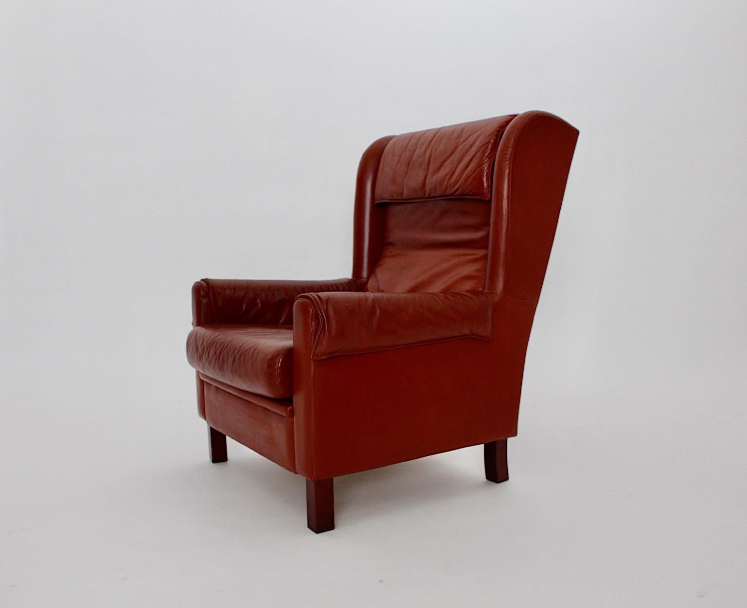 Leather vintage wingback chair or lounge chair from reddish brown leather 1970s Austria.
While the vintage wingback leather chair shows two loose cushions its feet are made from beech and walnut veneer.
The wingback chair or lounge chair is