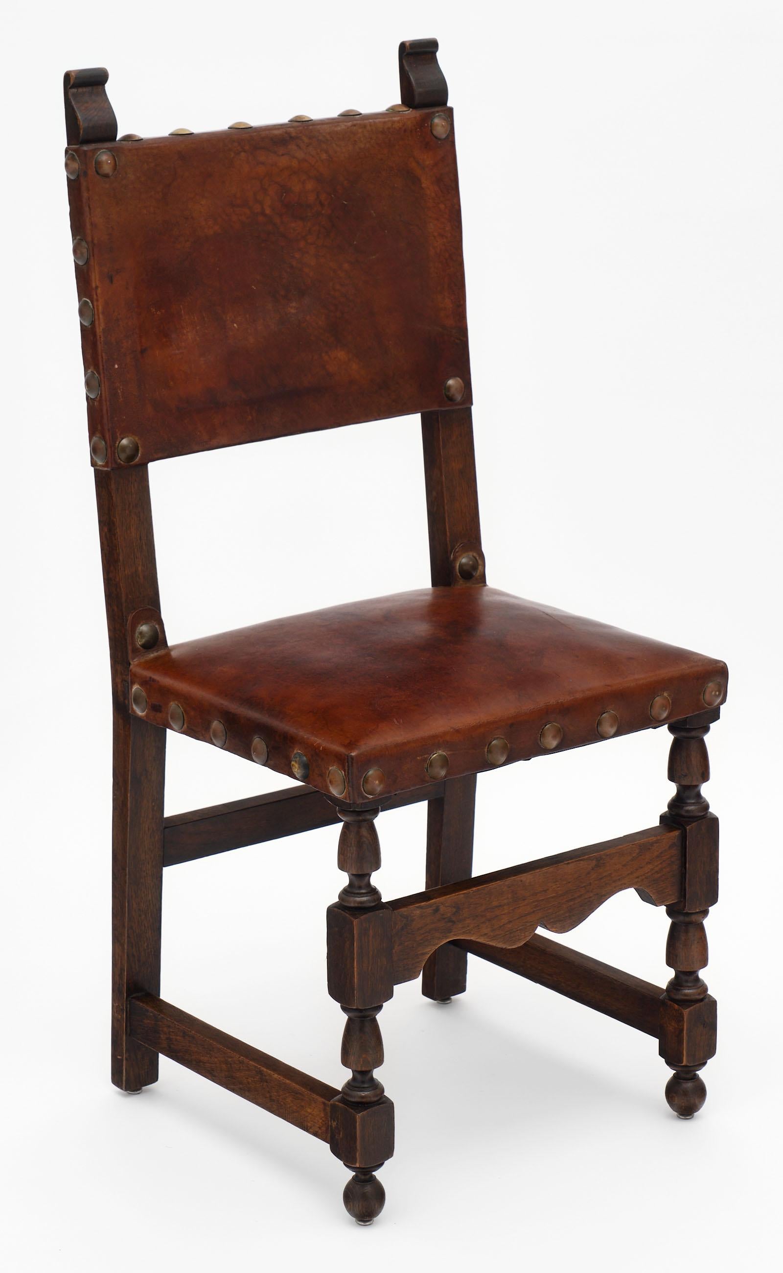 Rare set of ten Renaissance style leather dining chairs featuring hand carved wood, leather seats, and original brass studs. The front legs are beautifully turned and the seats are quite comfortable.
