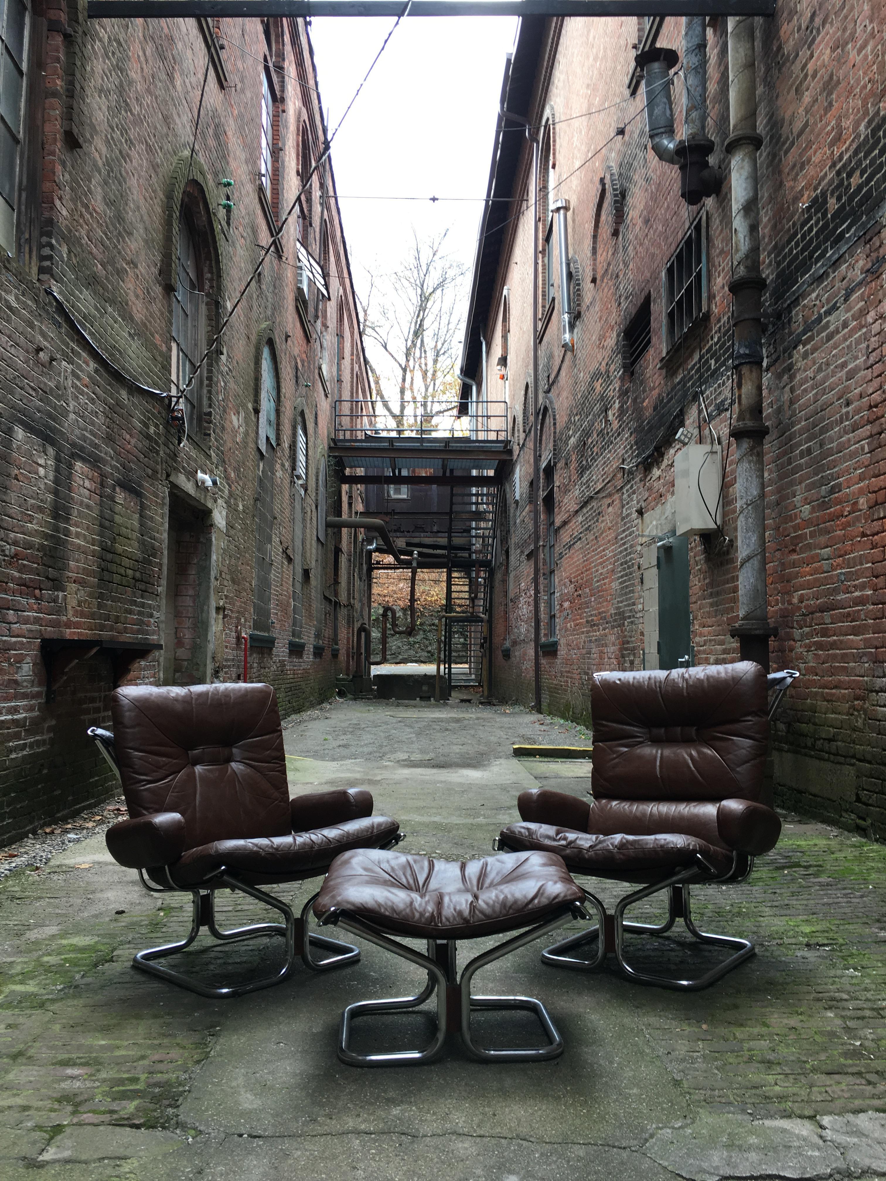 Two tubular chrome and rosewood sling armchairs for Westnofa, Norway. Designed by Ingmar Relling for Westnofa. Featuring chocolate brown leather cushions, tubular chrome frames with Rosewood accents. One chair has a slightly higher back cushion,