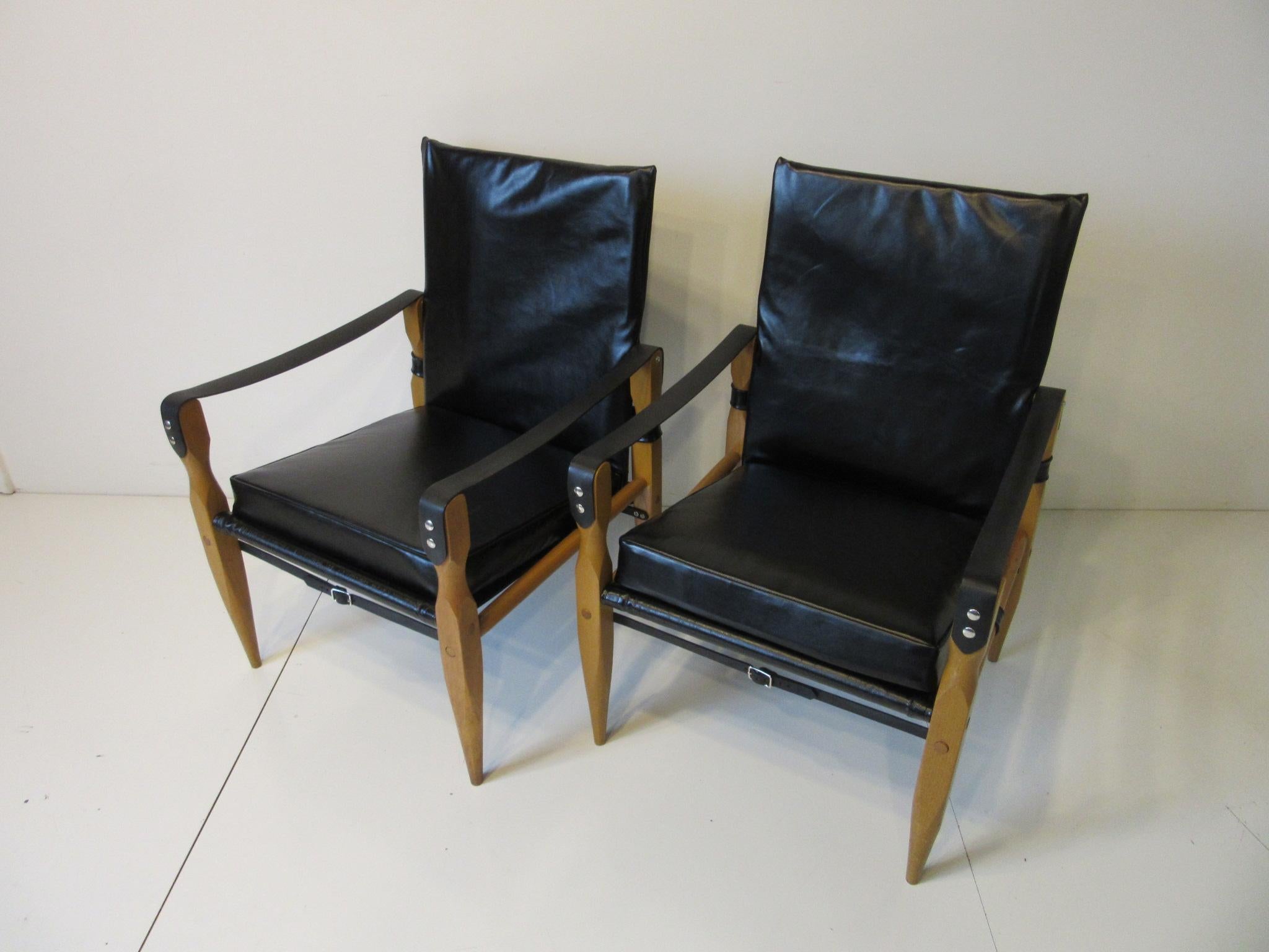 A beautiful pair of comfortable beechwood framed Safari chairs with mat black leather arms and straps with brass buckle detail. The seat back and bottom cushions are in a high sheen soft black leather giving these chair a sophisticated look and