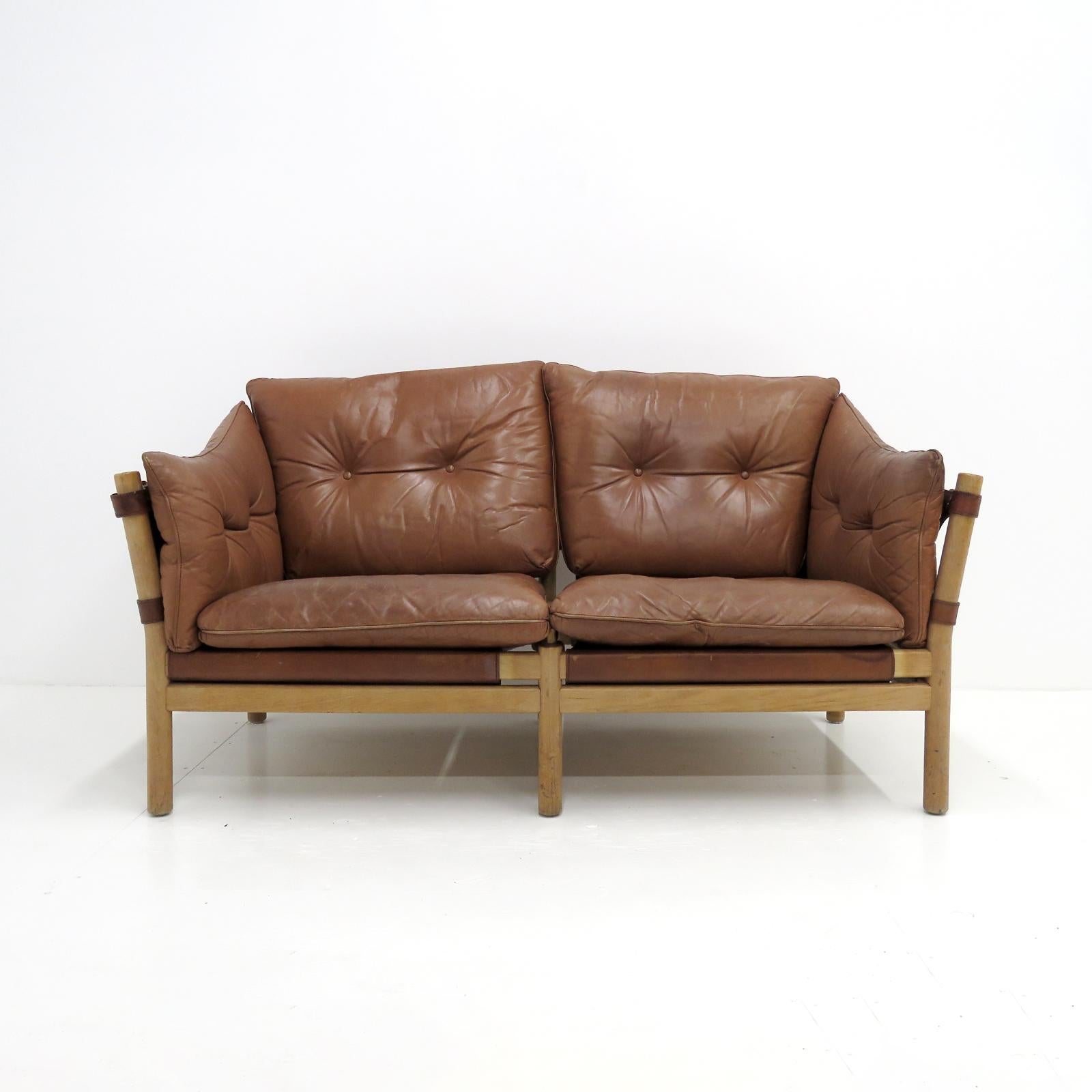 Stunning leather settee designed by Arne Norell in the early 1960s and produced by Aneby Møbler, Sweden, with thick, cognac colored leather cushions on saddle leather sling supports with brass hardware, the frame is made of sturdy, solid, beech,