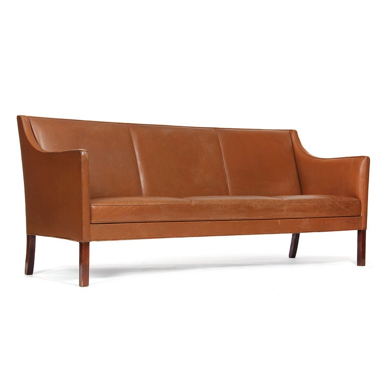 A sofa with a raised, tight back and sloping arms, retaining the original tan leather upholstery, on rosewood legs.