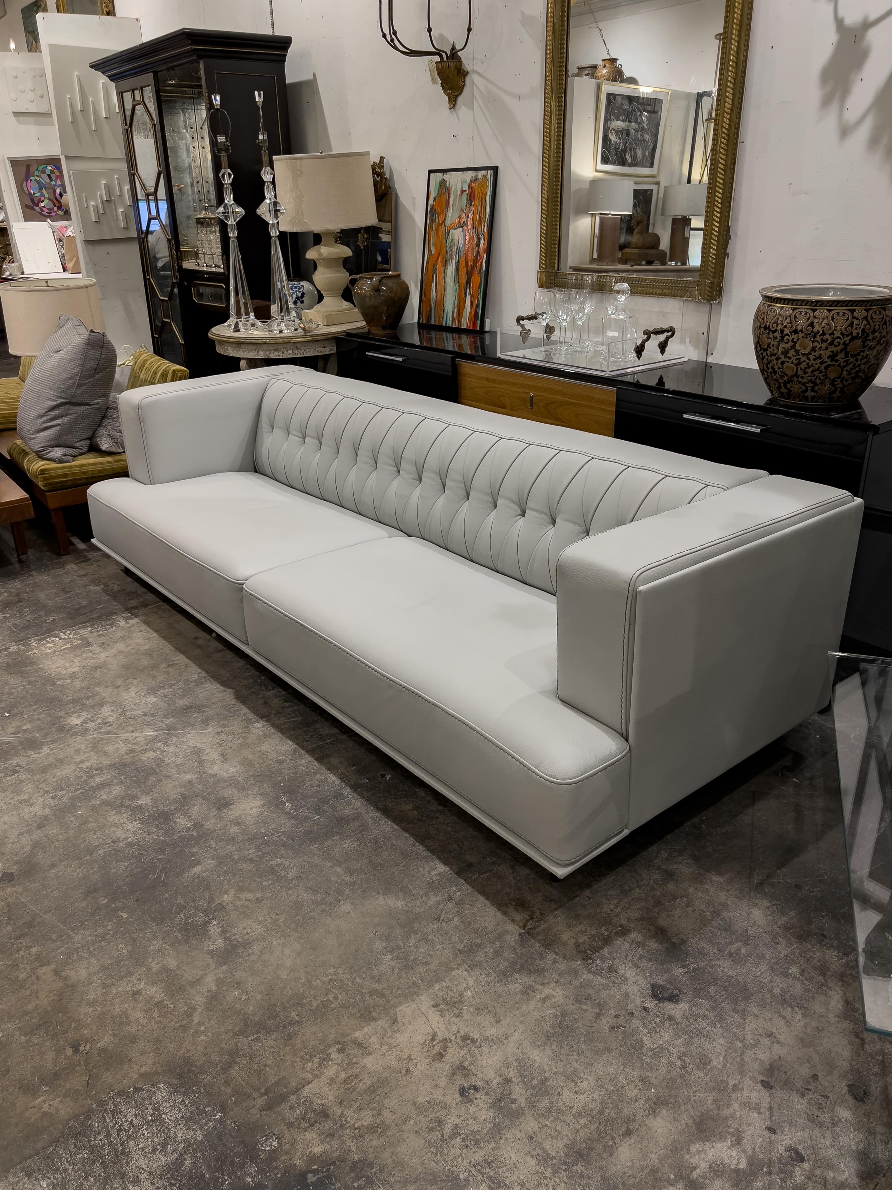 Grey Leather sofa with a tufted back, block arms, and two attached seat cushions. The couch is supported by 5 thin metal legs.