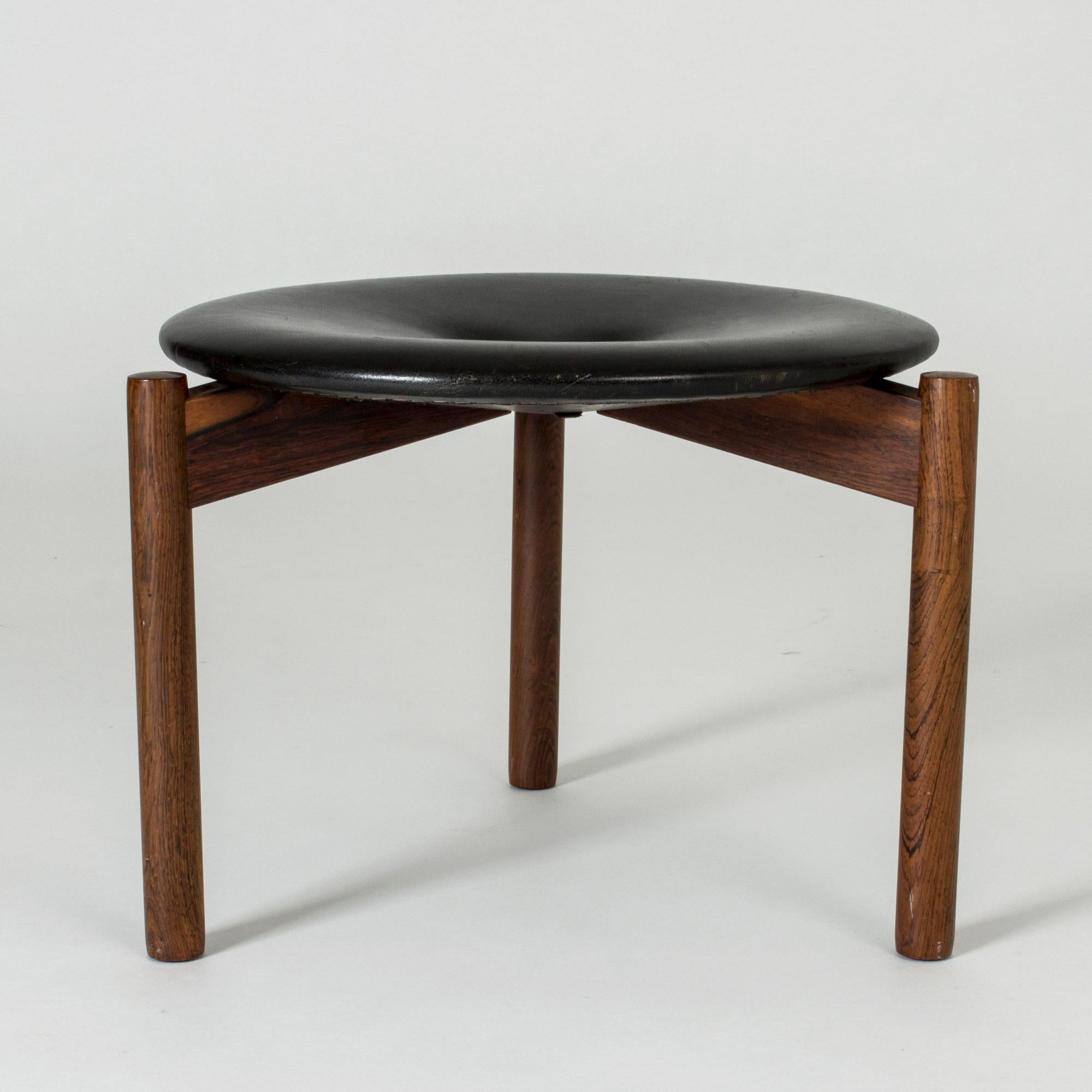 Neat round stool by Uno & Östen Kristiansson, with a tripod rosewood base and black leather seat. Nicely patinated leather, three leather buttons in the middle.