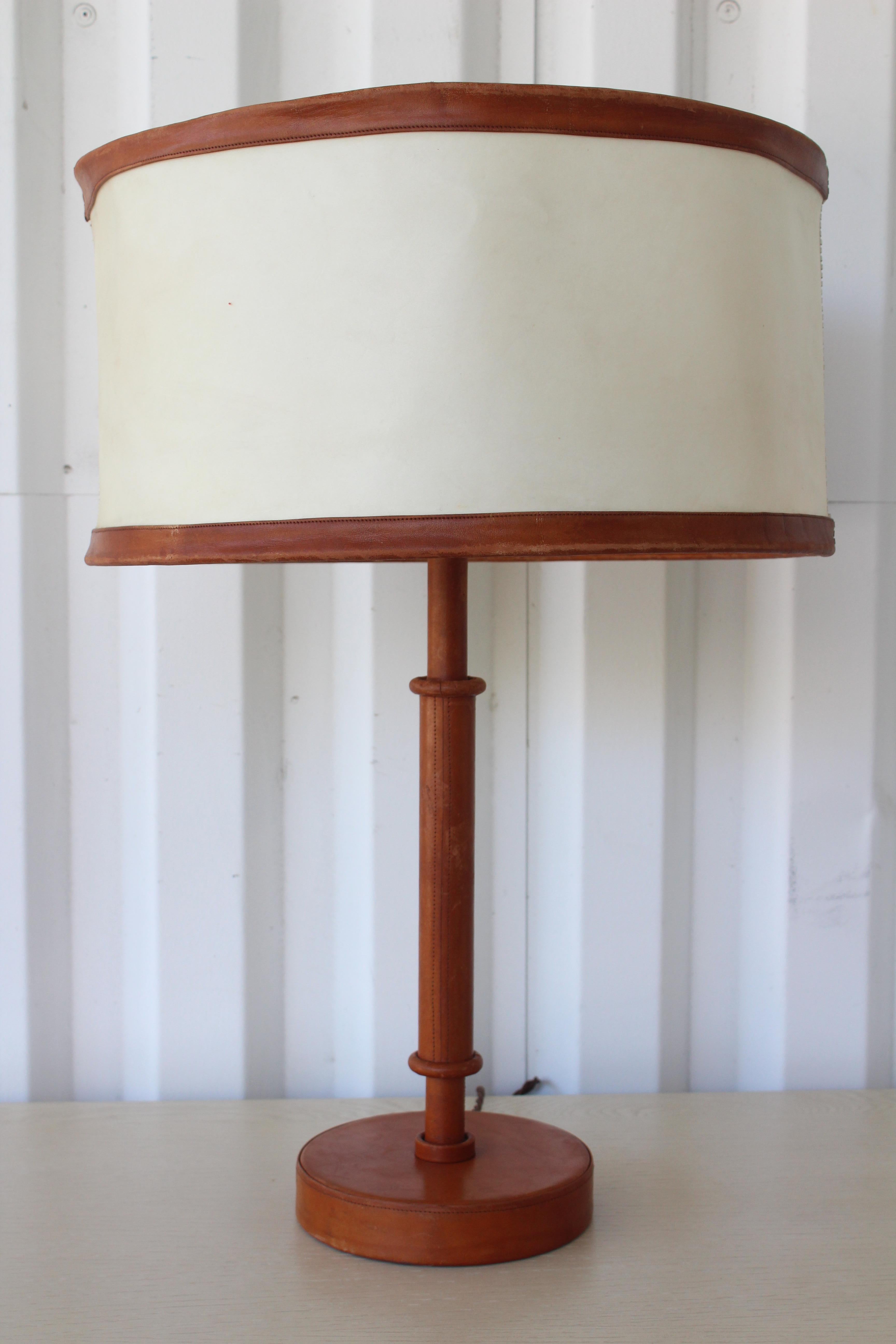 Vintage 1950s French leather wrapped table lamp designed by Jacques Adnet. Newly rewired. Includes original leather and pig-skin lamp shade as well as a custom shade in linen. The leather shows age appropriate wear and patina but has been condition