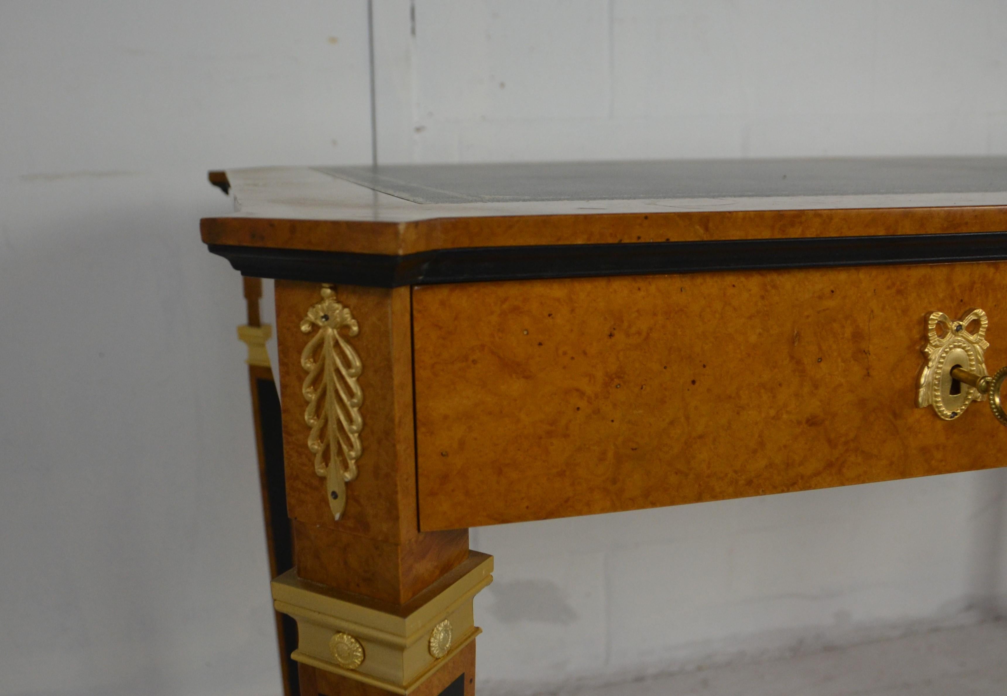 A leather topped burl-wood desk. A light colored burlwood finish with ebonized panels to the legs. Gilt metal decorations to drawers, back, legs and corners. Features a leather writing top with a gold decorated band.