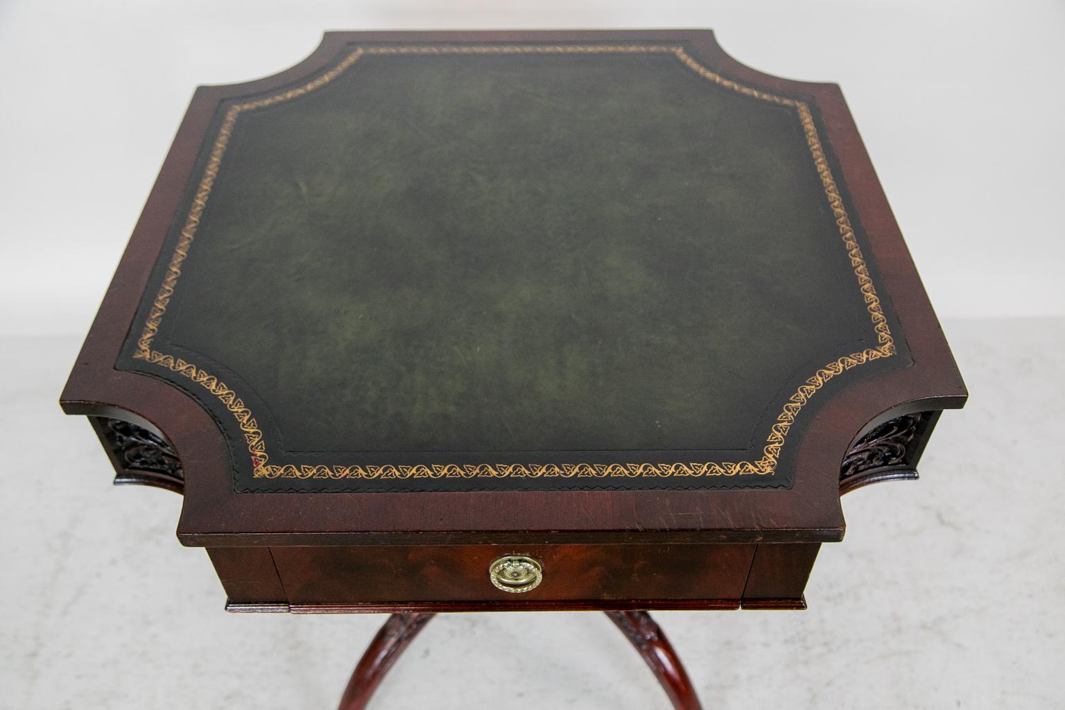 This American center table has a reverse quatrefoil shape. The concave corners of the apron are carved with stylized Prince of Wales plumes. The four arched legs are carved with stylized acanthus leaves and bell flowers. The green leather top has a