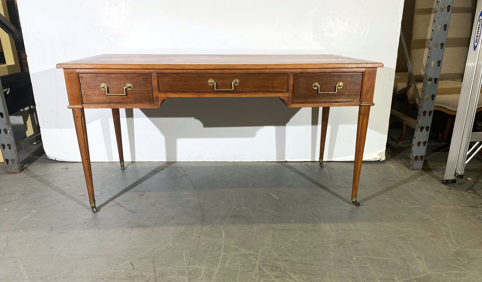 Leather top writing desk by Baker. Three drawers, brass pulls, and casters.