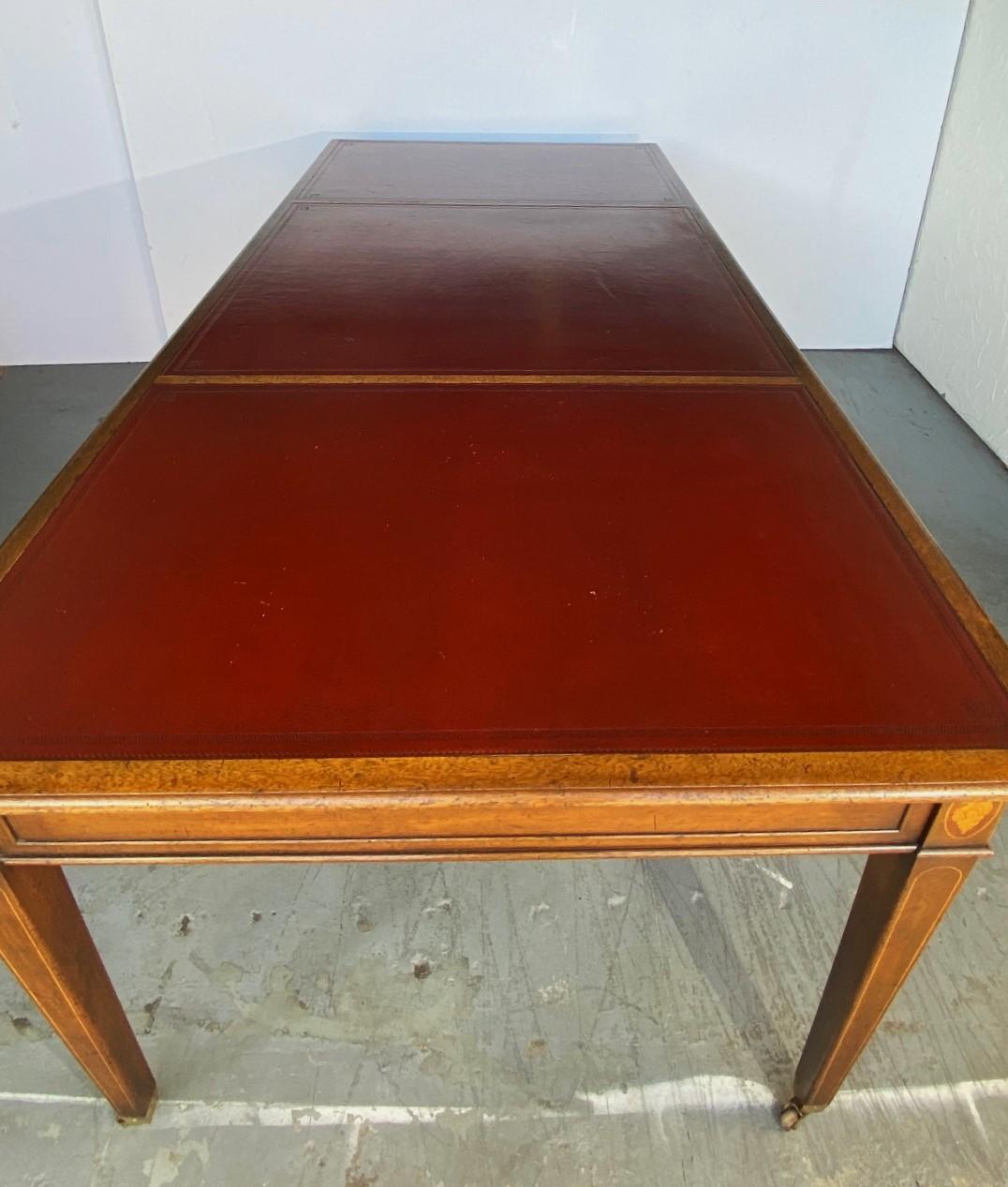 A leather top writing desk by Kittinger. One side has three drawers other side has three faux drawers. The legs have inlay details with brass casters.