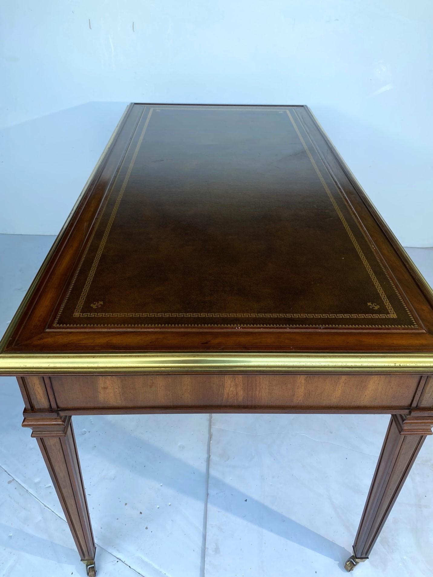 A leather top writing desk with brass accent on the edge and three drawers