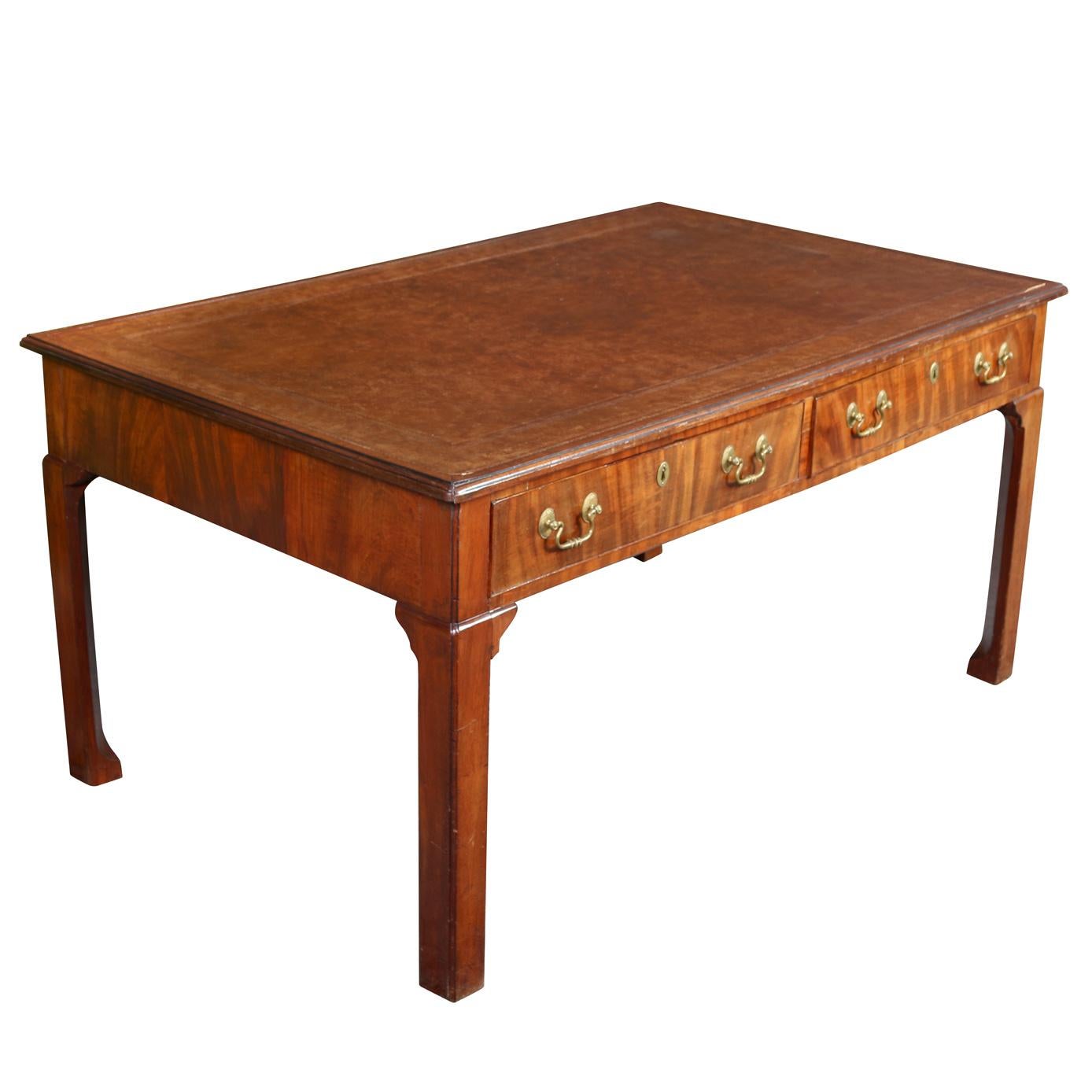 A Chippendale style writing desk with tooled brown leather top and two drawers, each with two hanging bale pulls and a single keyhole. The desk features Ming style feet, straight legs with small fretwork at the top. An elegant addition used as a