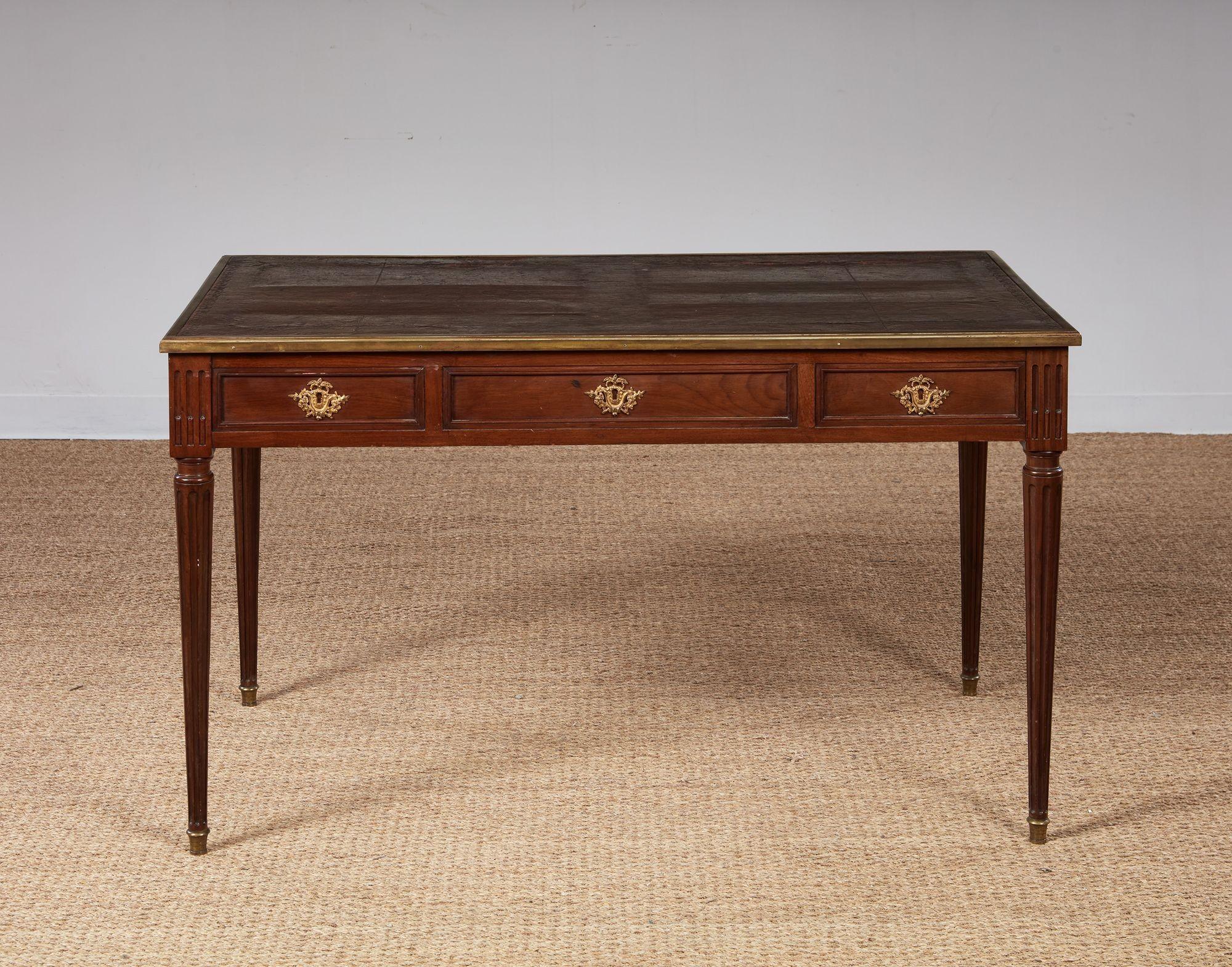 French Louis XVI walnut writing table, the leather surface with molded brass trim over three oak lined drawers, retaining original gilt bronze laurel and vine hardware, with pull-out slides to the ends, and standing on turned fluted legs with