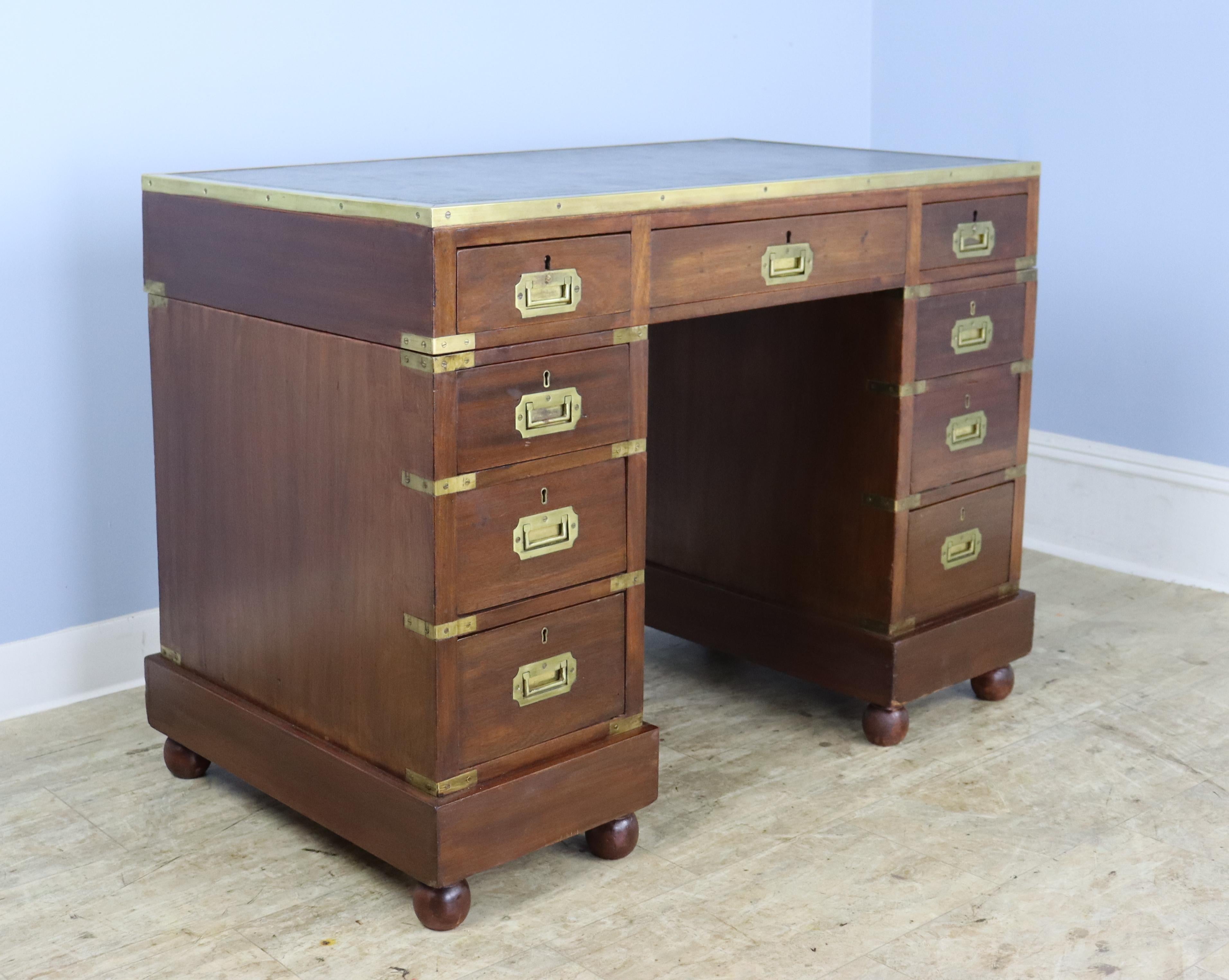Theres alot to admire about this beautiful original campaign desk. Both the mahogany and the original green embossed leather are in good antique condition, as are the brass accents. The interior of the drawers are clean and the sweet bun feet are an