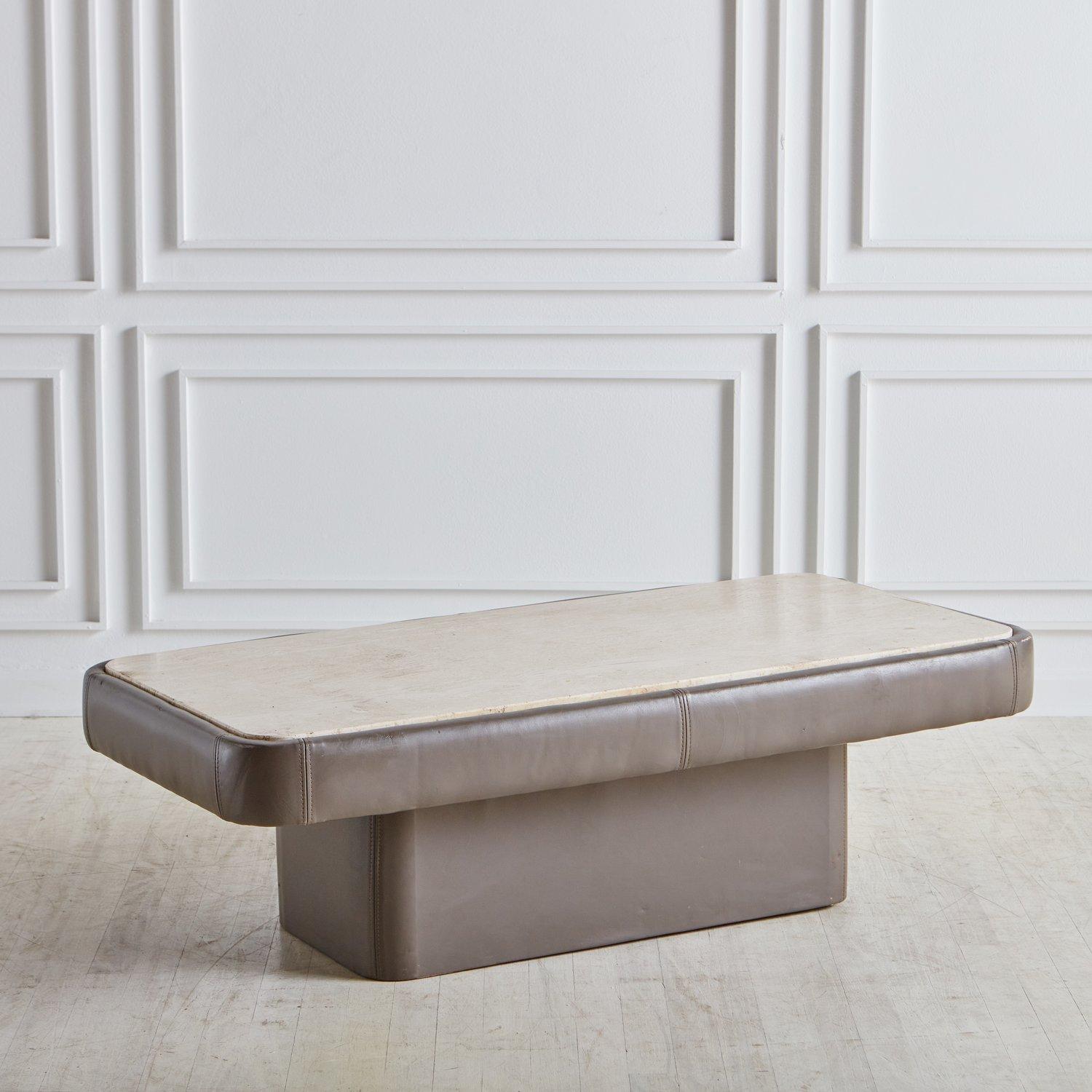 A beautiful vintage coffee table attributed to De Sede featuring a gray leather clad frame with a rectangular pedestal base and stitch detailing. This piece has an inset travertine table top with rounded corners and elegant veining. Sourced in