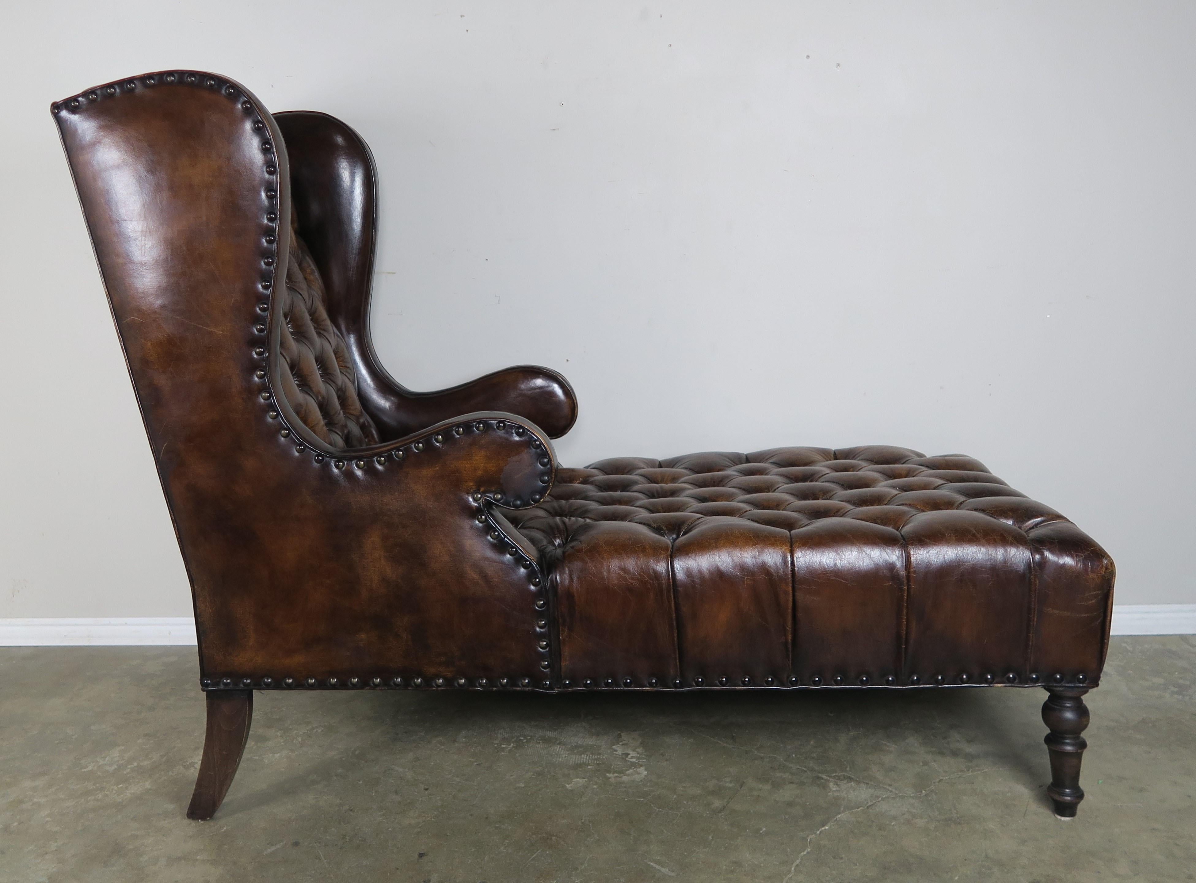 Leather tufted wingback chaise with nailhead trim detail. The chaise stands on four turned legs finished in a dark walnut coloration. Self cord and flat welt detail finished with large size antique brass nailhead trim detail.
Measures: SH 18