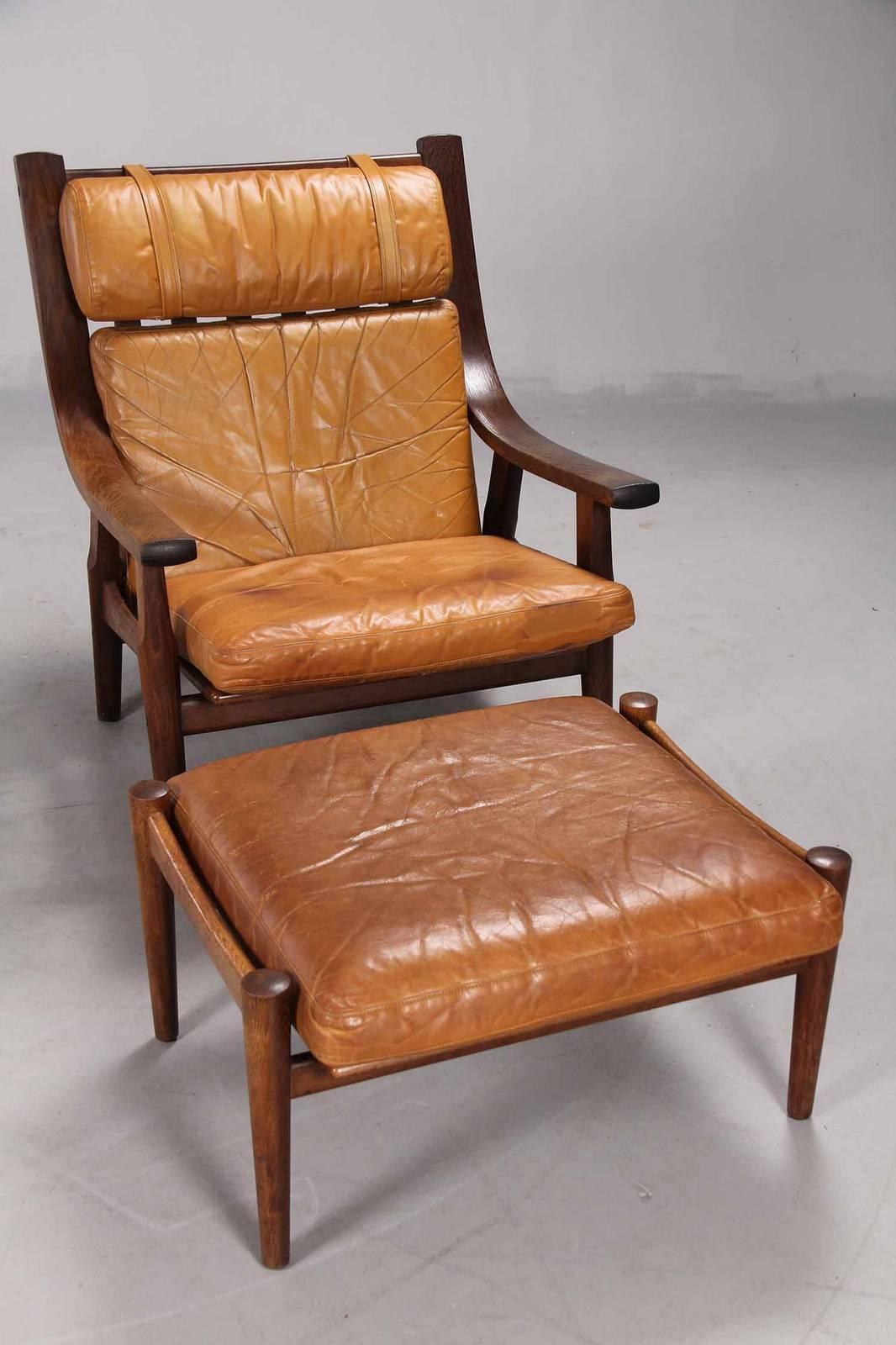 High-backed armchair and ottoman designed by Danish Designer Hans Wegner in 1973. The frame of dark-stained oak with spoke back, both the chair and ottoman upholstered in cognac-colored leather. The chairs produced by GETAMA, model GE-530.