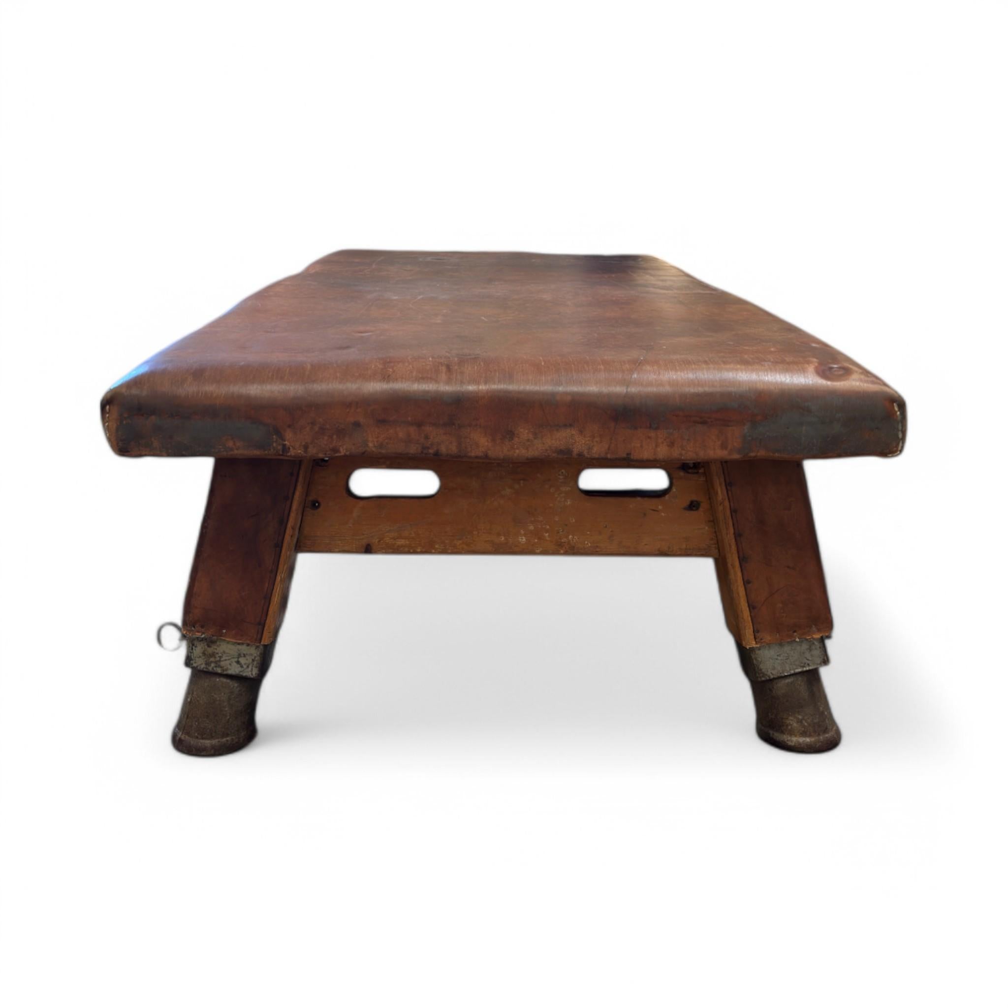 This vintage pommel horse has been thoughtfully repurposed into a striking coffee table. Its rich, timeworn leather top exudes character, while the sturdy wooden base and original metal-capped legs add to its industrial charm. A perfect blend of