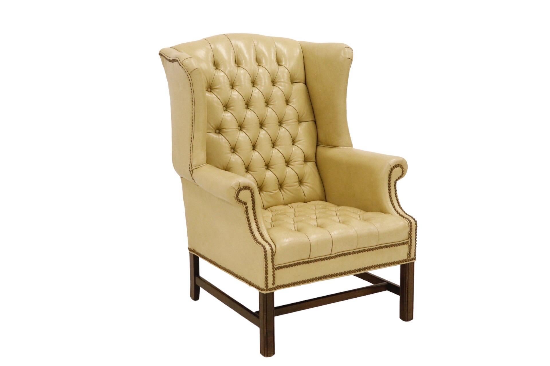 A leather tufted Chippendale wingback in cream. Diamond button tufted on the inside back and seat, secured on rolled arms, across the front skirt and around the base with a brass nailhead trim. Straight square legs with a beveled line detail are