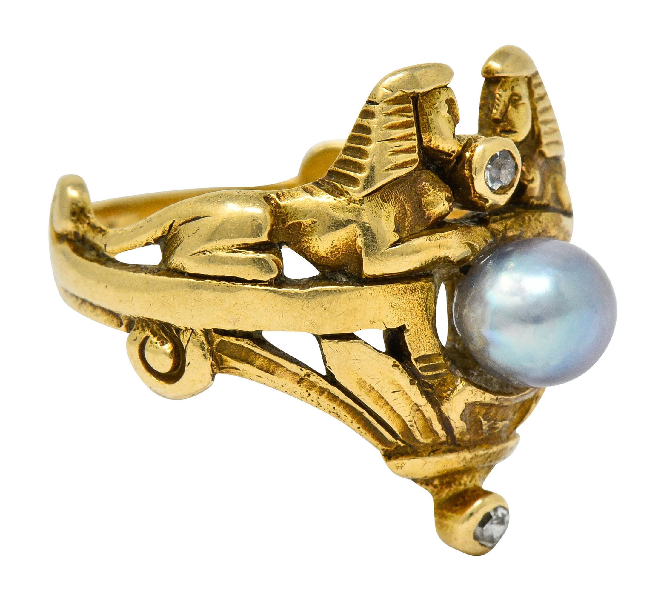 Band style ring is designed as two mirrored Sphinx with a stylized lotus base

Centering a semi-round 5.6 mm pearl, gray in body color with slight green/purple overtones and good luster

With engraved and scrolled whiplash details accented by bezel