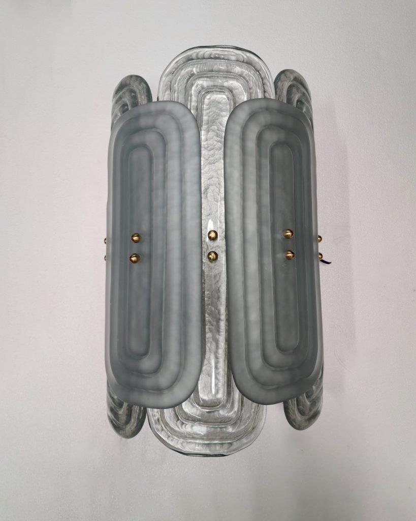 Italian Murano Wall Sconces made by eModerno, meticulously created in Italy to meet the highest standards of quality.
Featuring two distinct sizes of rectangular glass securely affixed to a semi-circular frame adorned with brass details, these wall