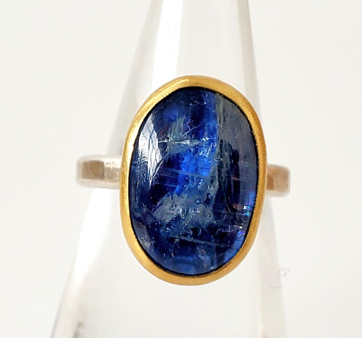 Solitaire ring featuring a deep, marine blue oval kyanite cabochon; hand set in a 22K gold bezel, sterling silver back and band. Blue kyanite: 9.4 carats. Size 6.

he Metaphysical Particulars: Blue kyanite helps to rebalance one’s energy and is